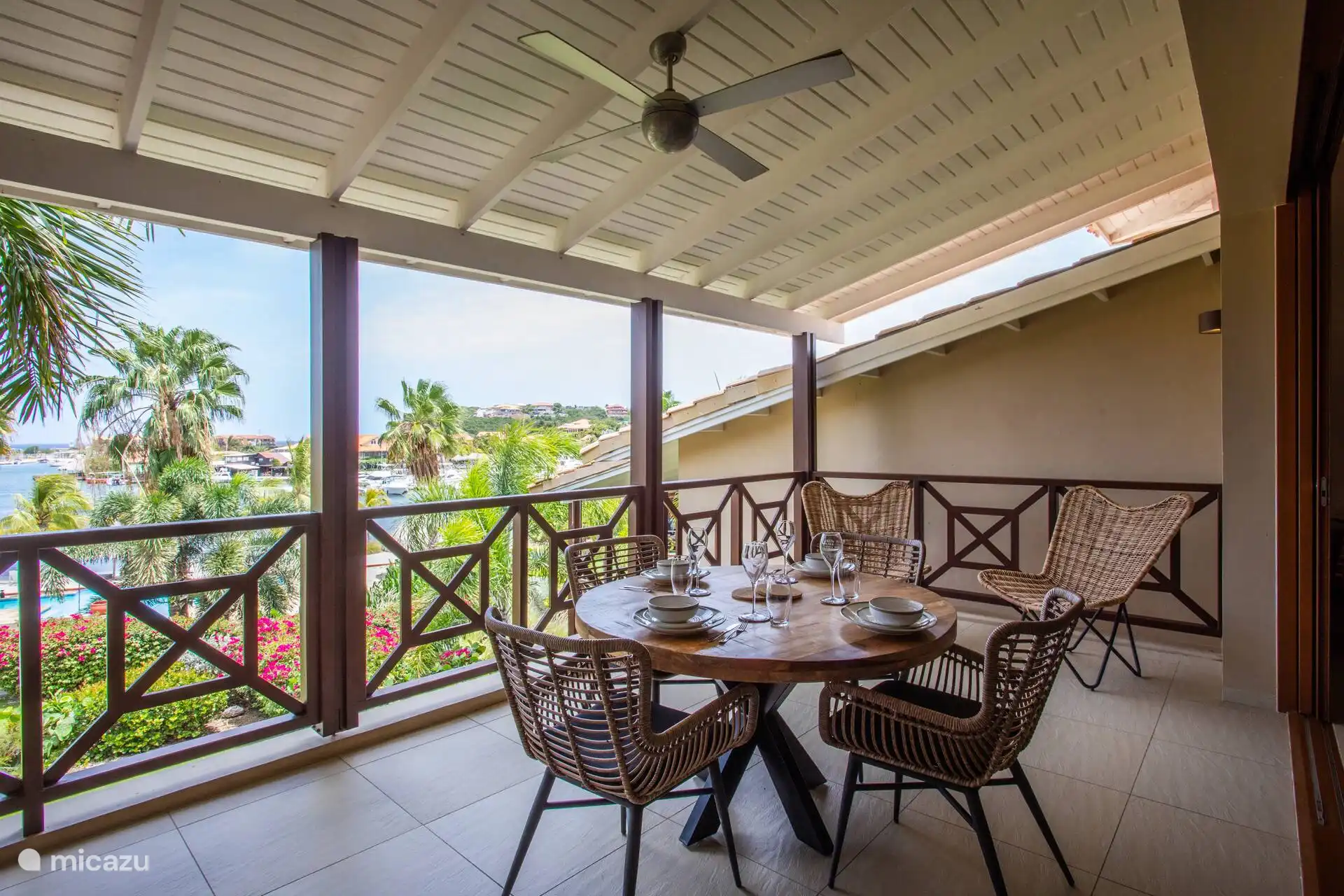 Geräumiger überdachter Balkon mit Esstisch und Ventilator. Ideal, um tagsüber bequem draußen zu sitzen, mit Aussicht und angenehmer Brise.