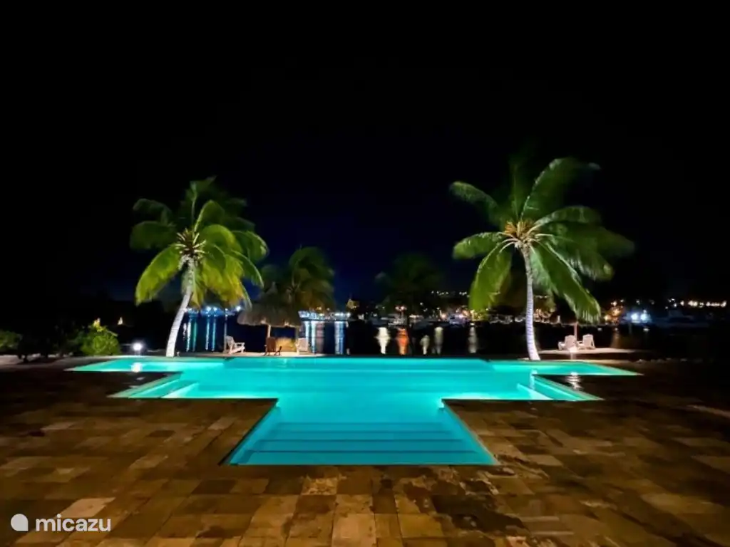 Abends ein schön beleuchtetes Schwimmbecken, mit Blick auf Palmen und das spanische Wasser.