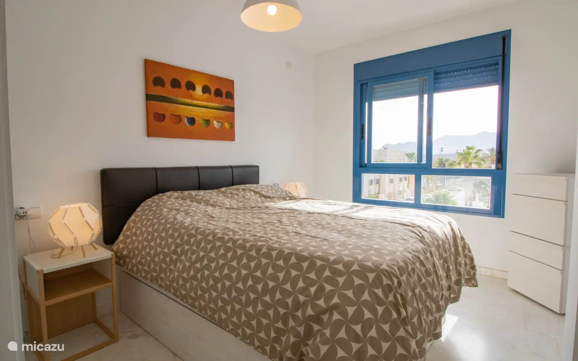 Een lichte slaapkamer met een tweepersoonsbed, nachtkastjes en een kleine en grote losse kledingkast