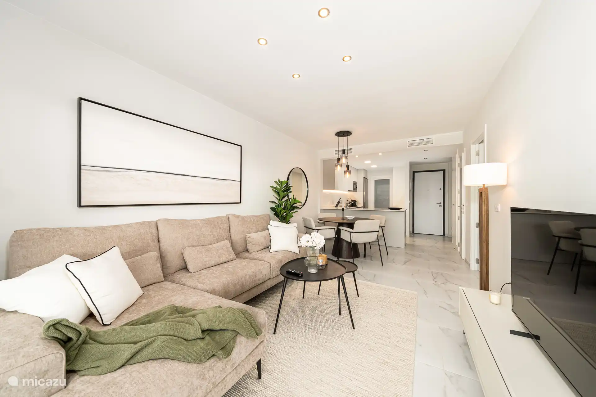 Lichte woonkamer met beige bank, zwarte salontafels en grote schuifpui naar zonnig terras met poolzicht.