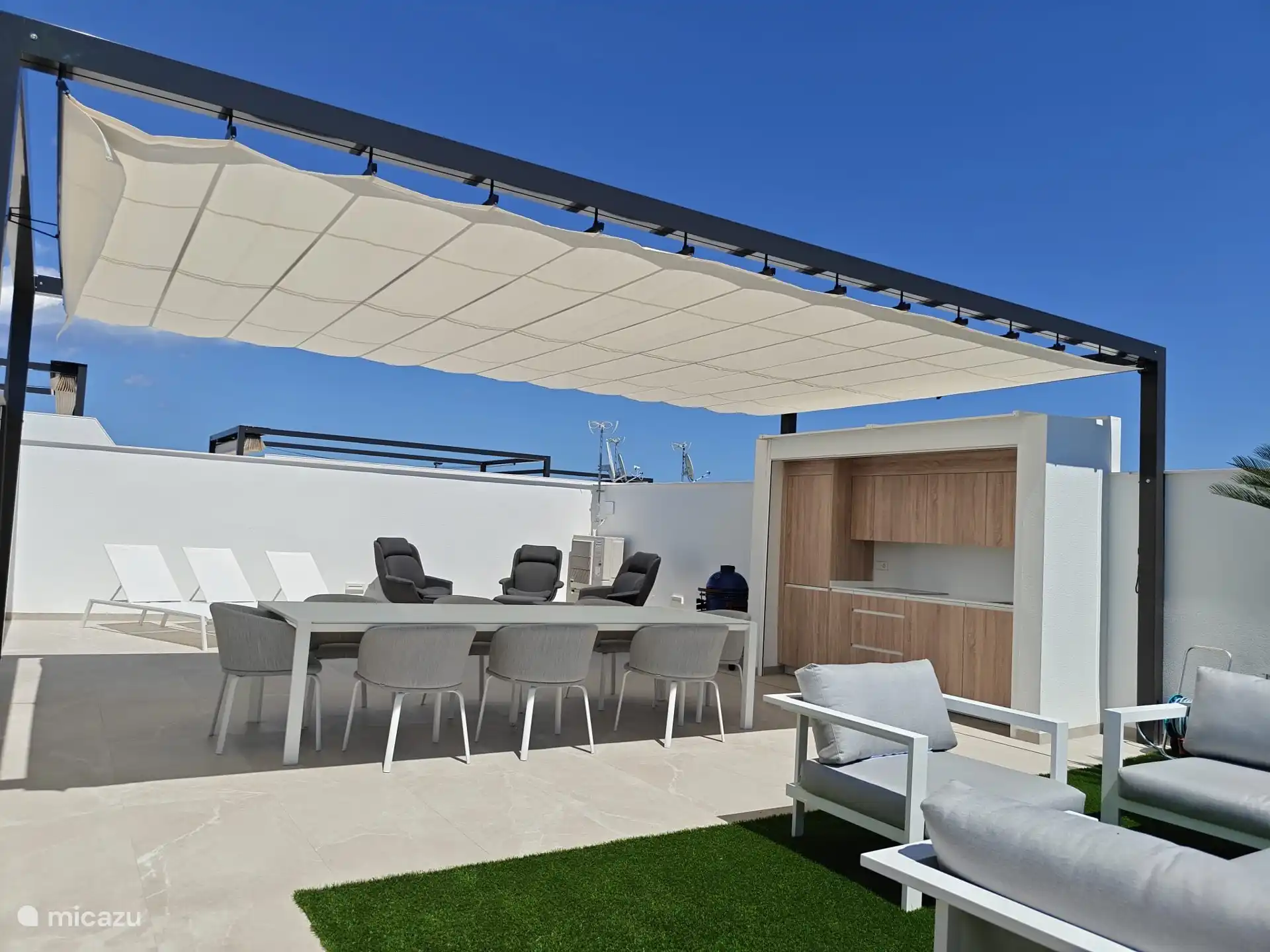 Terraza en la azotea con salón, cocina exterior con todos los electrodomésticos y equipada con utensilios tipo cala, mesa de comedor con sillas y tumbonas. 