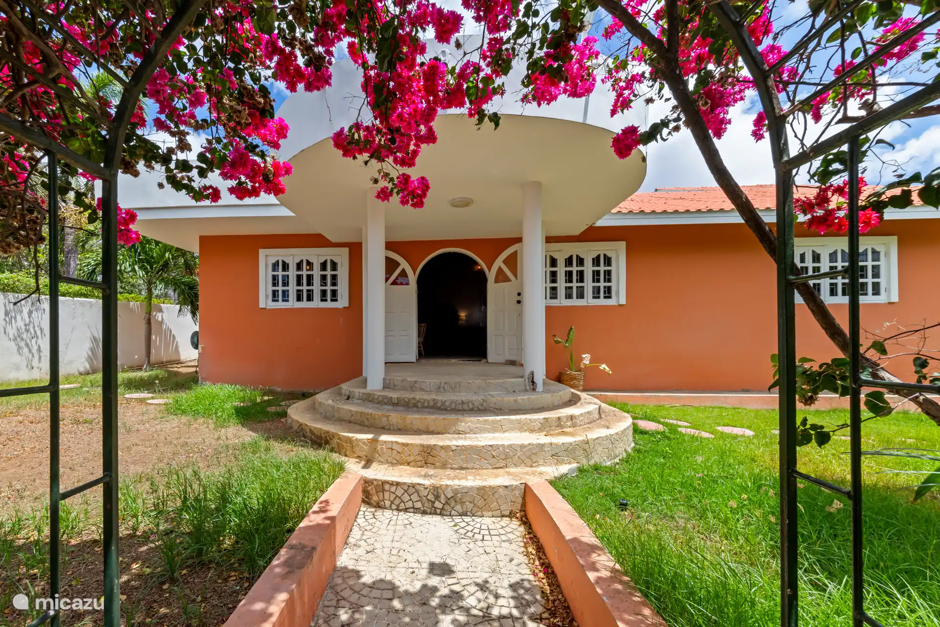 Entrée de la villa, entourée de verdure tropicale et de fleurs.