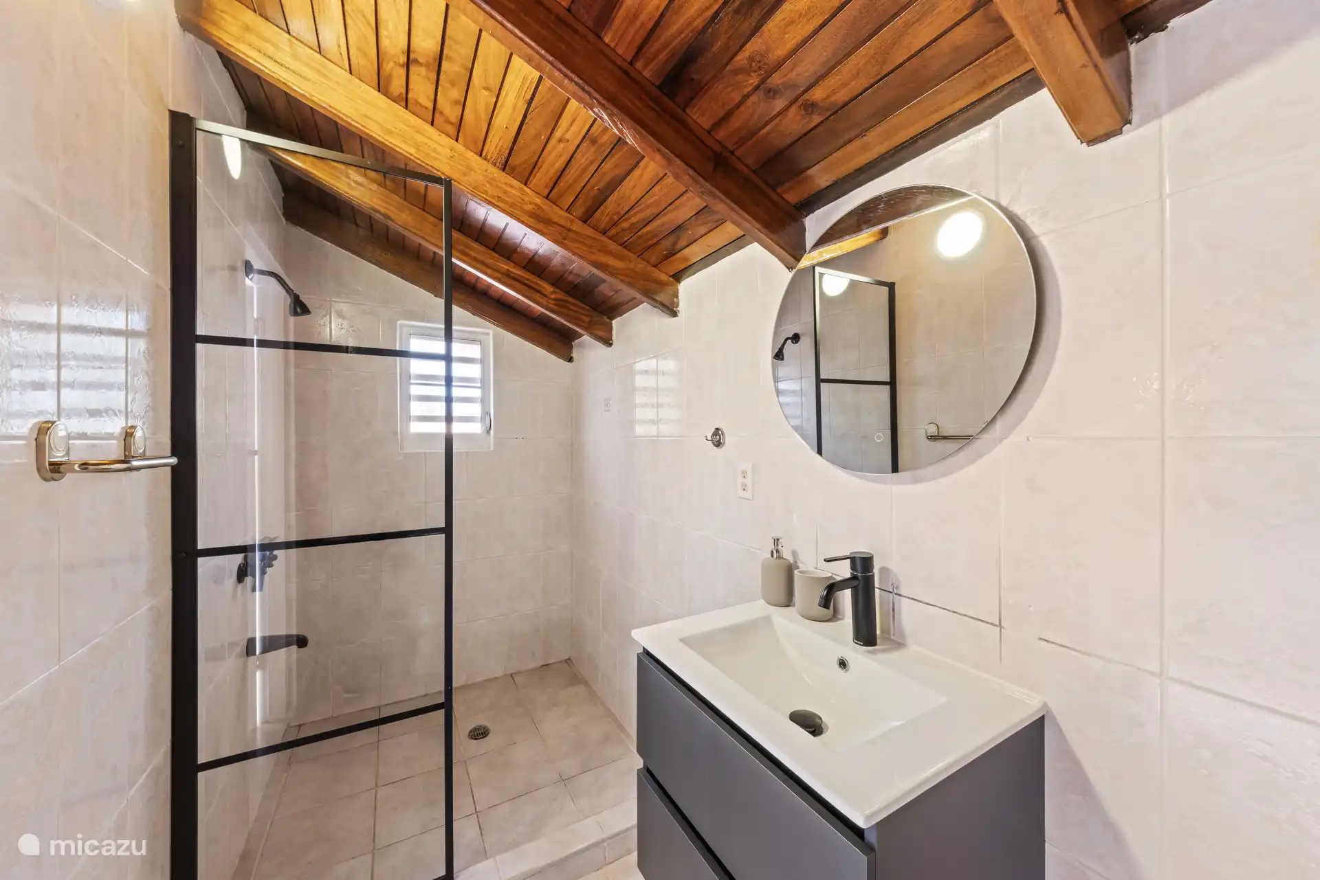 Salle de bain avec douche, lavabo et miroir rond.