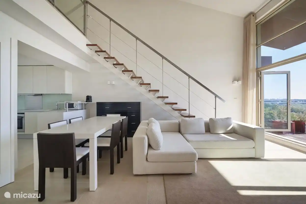 De woonkamer heeft veel lichtinval en is modern ingericht. De trap geeft toegang tot de bovenverdieping waar een badkamer is gevestigd en een dakterras met jacuzzi. 