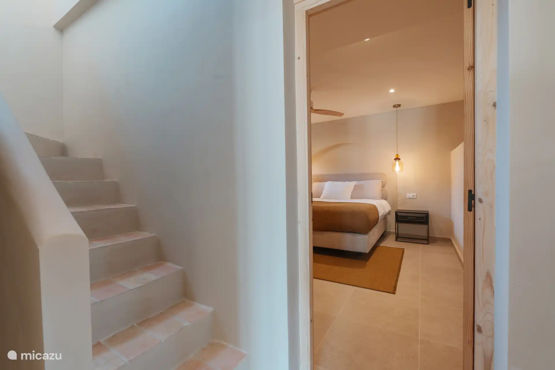 Escalier descendant au sous-sol avec une chambre de luxe très spacieuse avec un lit double fixe de qualité hôtel haut de gamme.