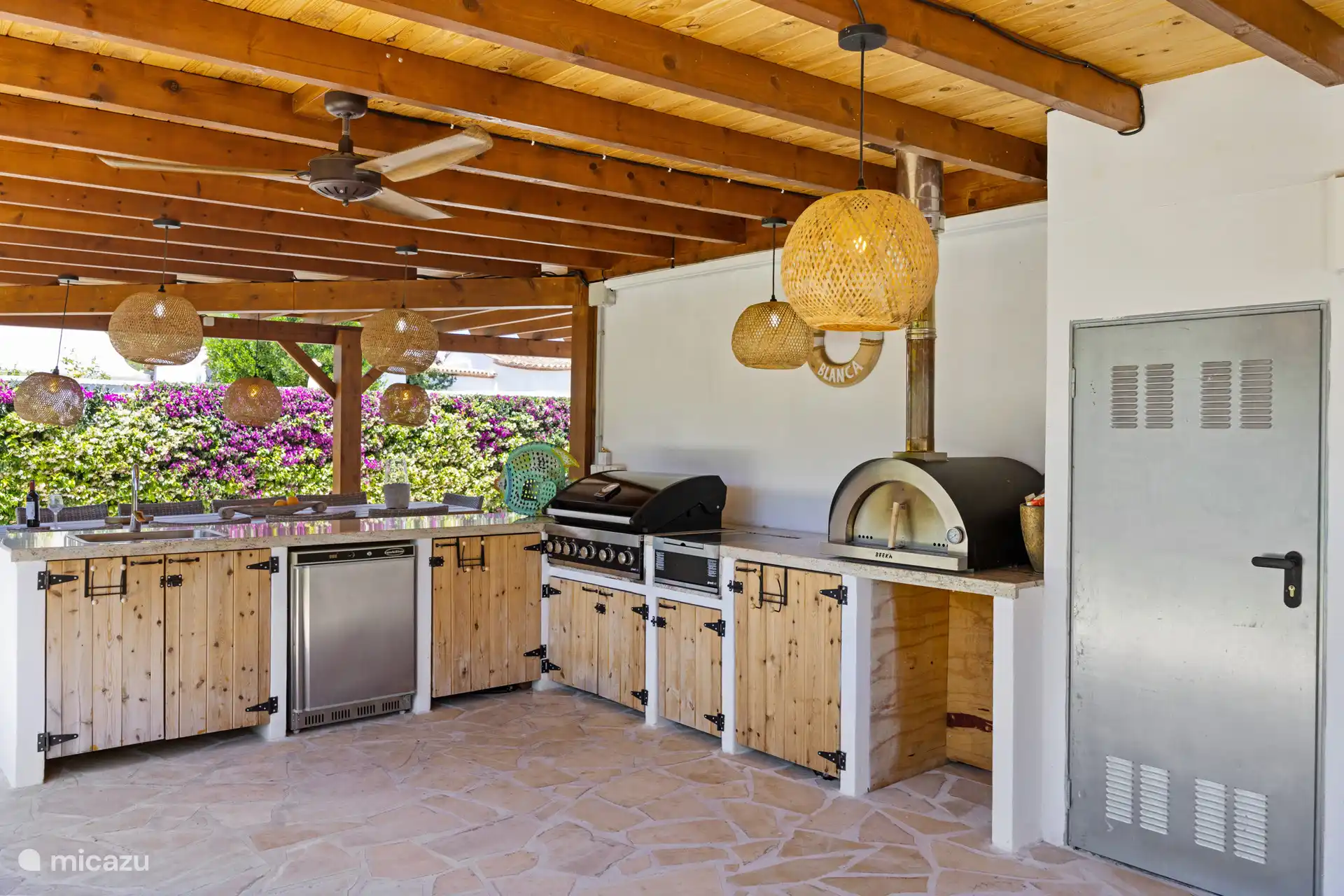 De buitenkeuken is een droom – pizzaoven, gasbarbecue en koelkast onder de pergola. Buiten koken met de bougainville in bloei. Vakantiemagie op z'n best.