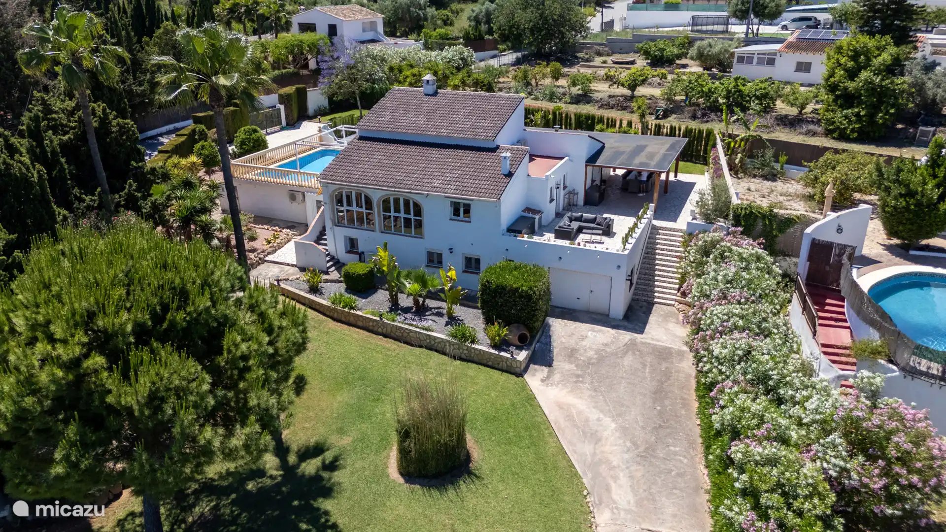 De villa met overdekt terras en loungehoek – omgeven door bloeiende tuin en groen. Hier begint elke ochtend goed.