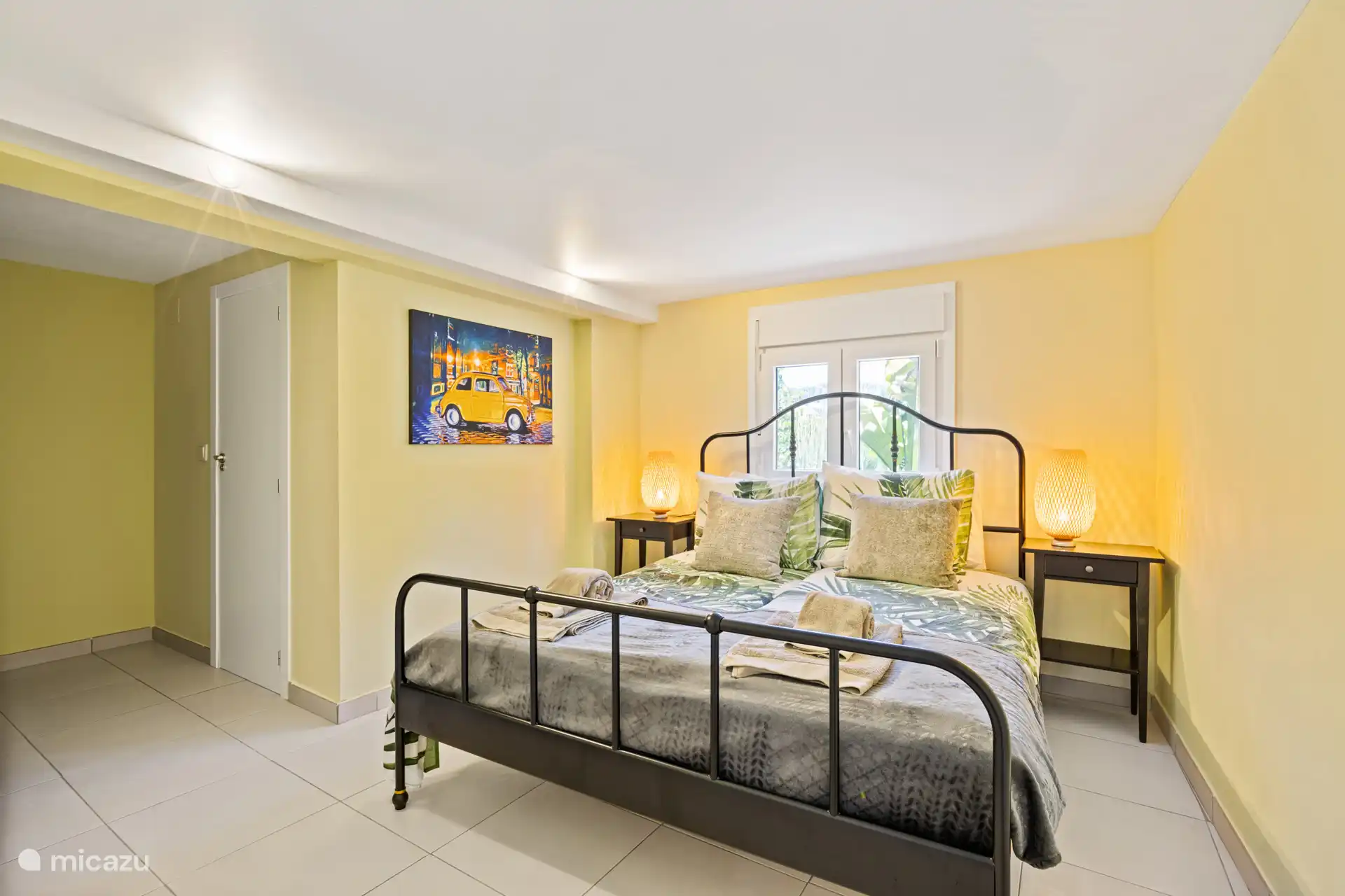 Rustige slaapkamer met sfeervol smeedijzeren bed en zachte tinten – de perfecte plek om helemaal tot rust te komen na een dag vol zon.