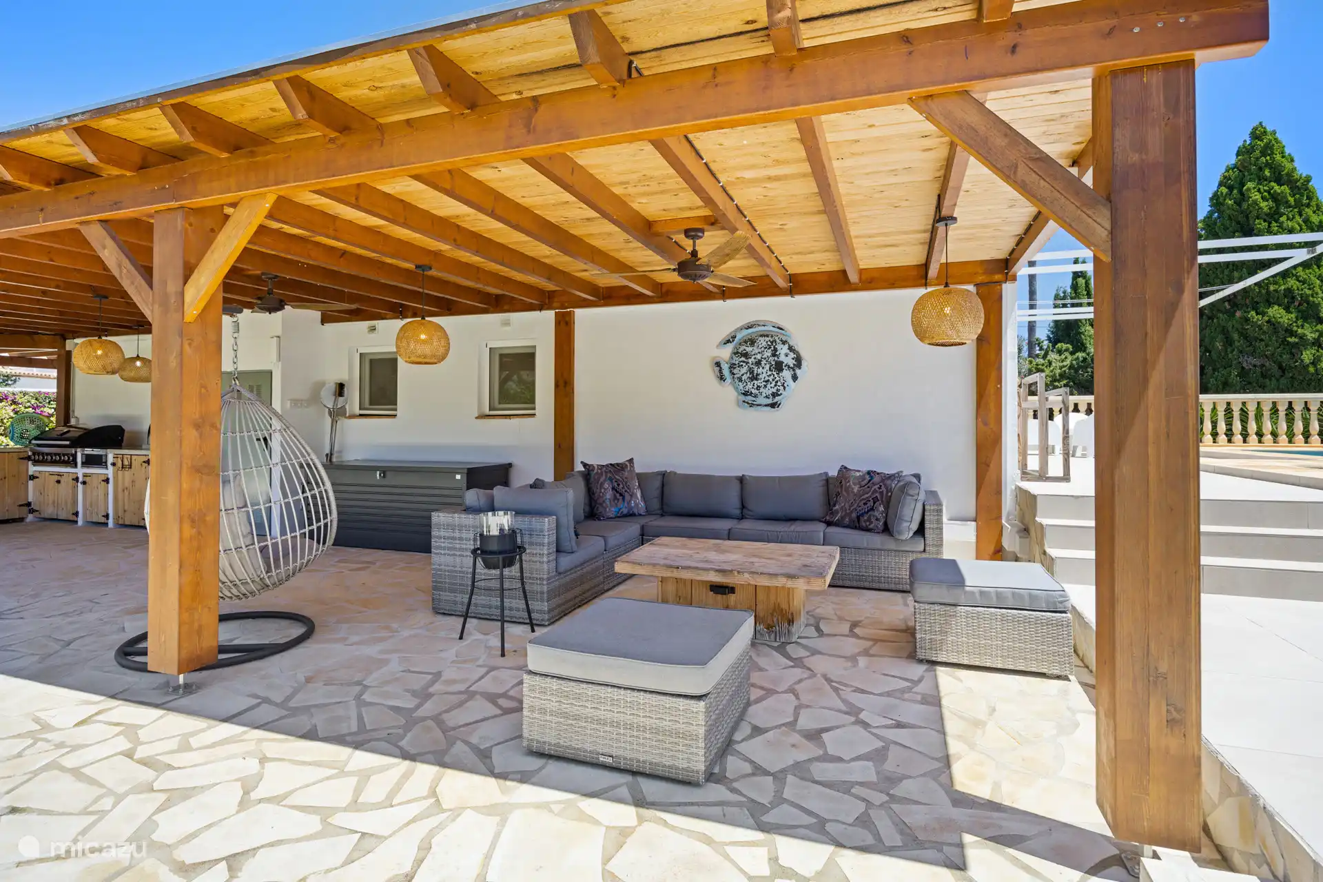Overdekt terras met houten pergola, loungebank en hangei – uw favoriete plek voor een kop koffie 's ochtends of een glas wijn als de zon ondergaat.