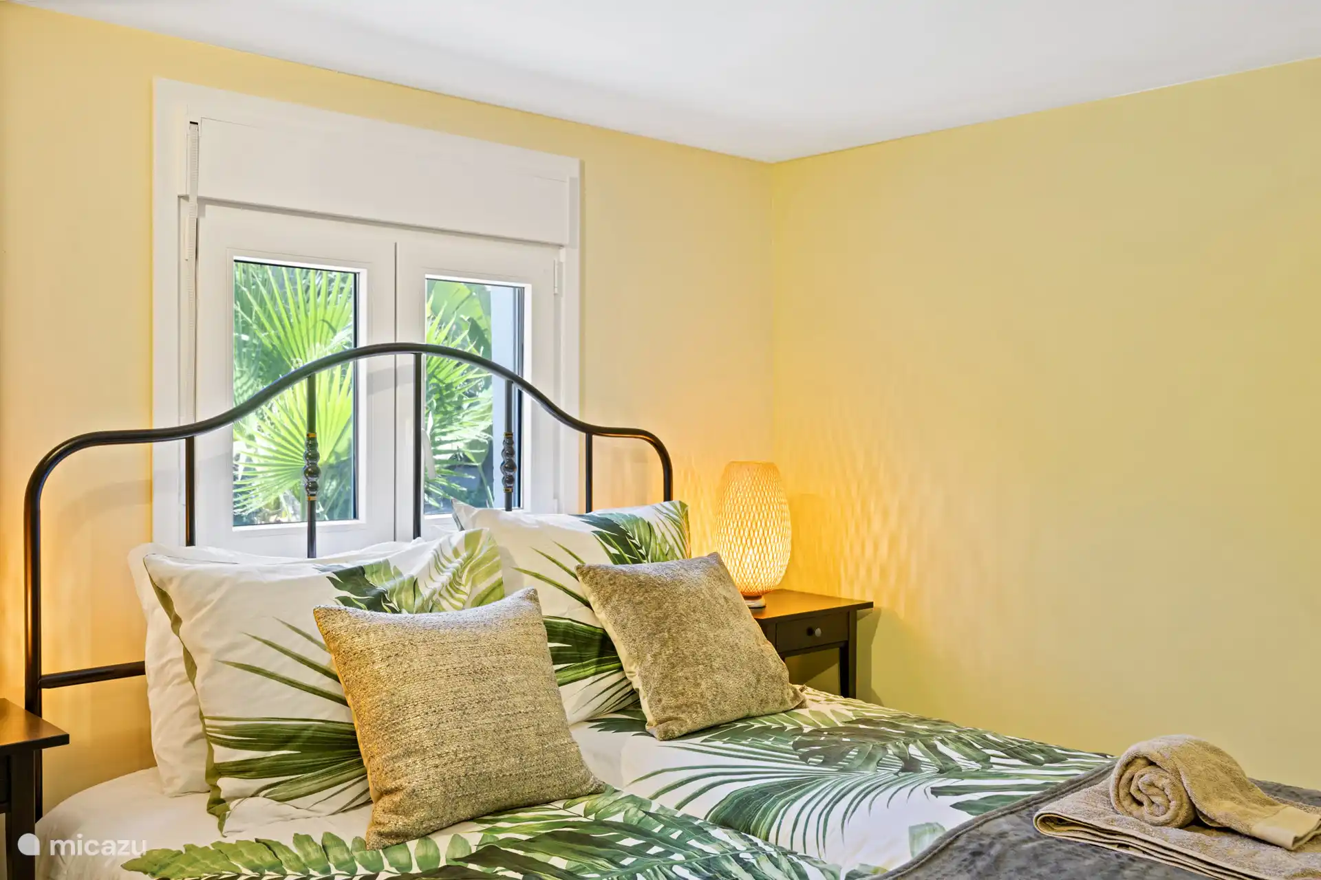 Tropische slaapkamer met palmbladeren print en uitzicht op de tuin – warm, sfeervol en precies het vakantiegevoel waar je naar op zoek bent.