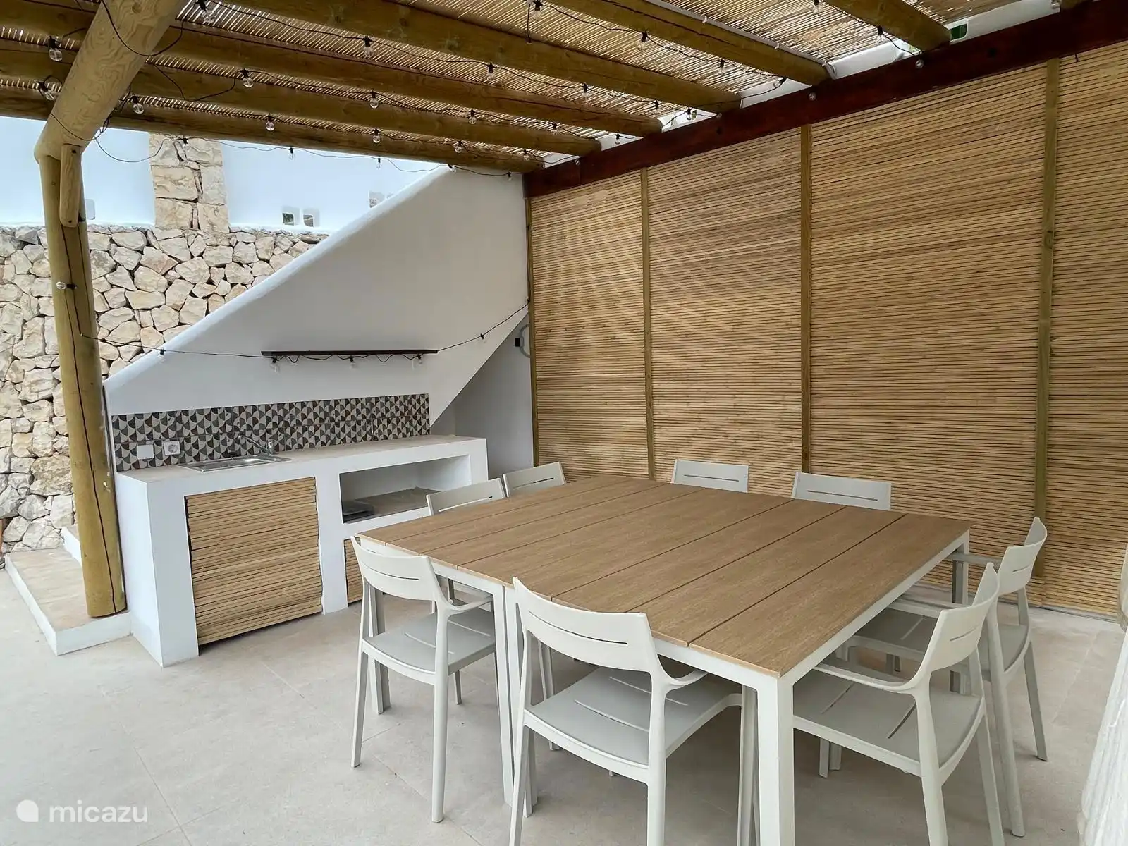 Cocina exterior bajo la pérgola con una hermosa mesa de comedor para cenar juntos. 