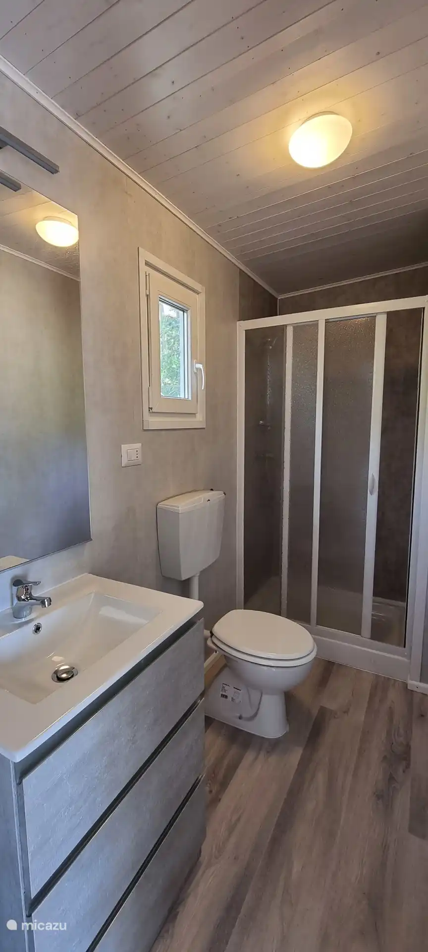 De badkamer heeft een wastafelmeubel om al je spulletjes in op te bergen. Een ruime douche, een toilet, en in een nis een wasmachine