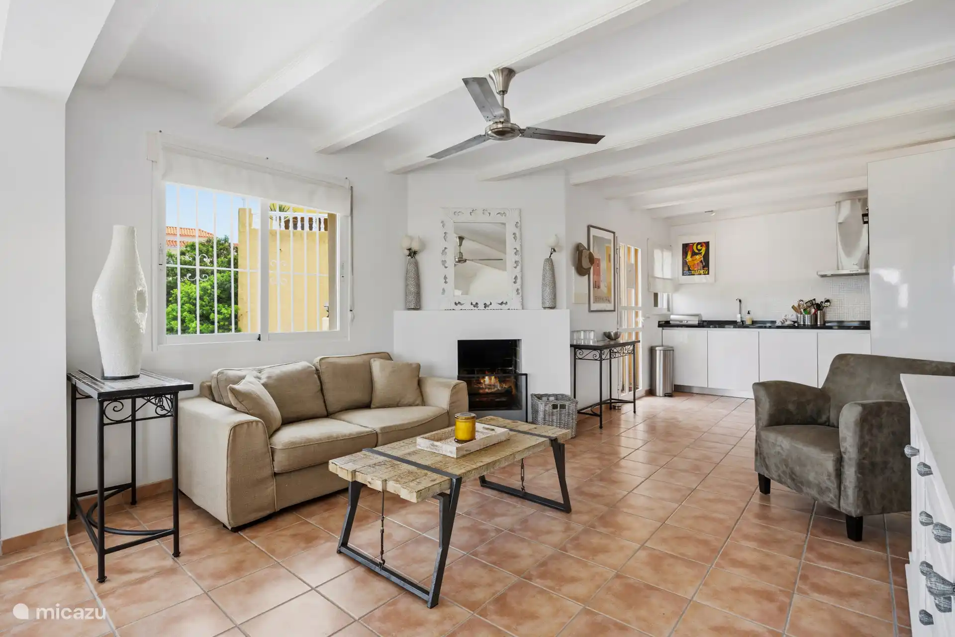 Appartement à l’étage — deuxième coin du salon avec cheminée, ventilateur de plafond et vue sur la cuisine. Spacieux et lumineux.