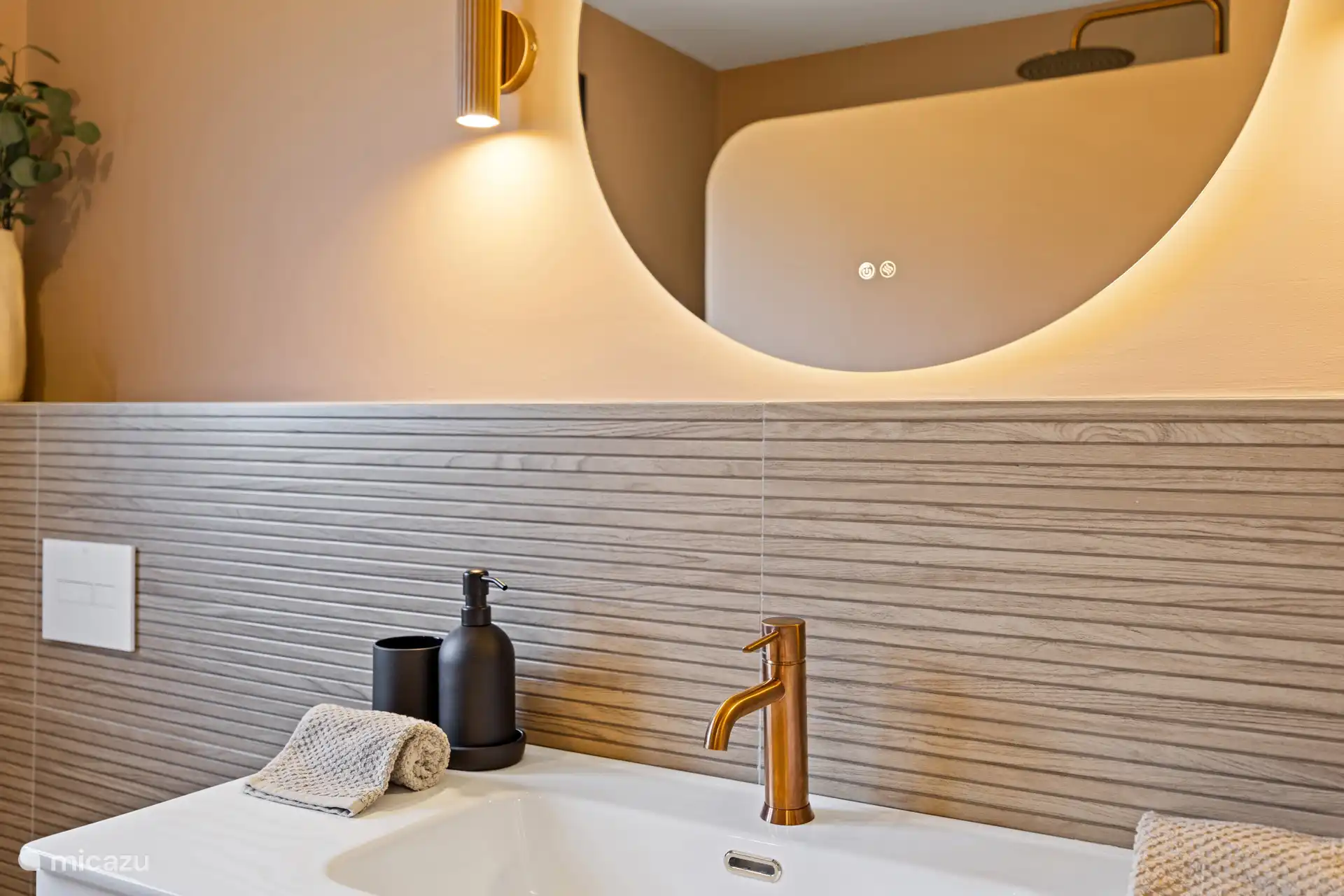 Verzorgd badkamerdetail met warme verlichting en natuurlijke materialen — de kleine luxe die het verschil maakt