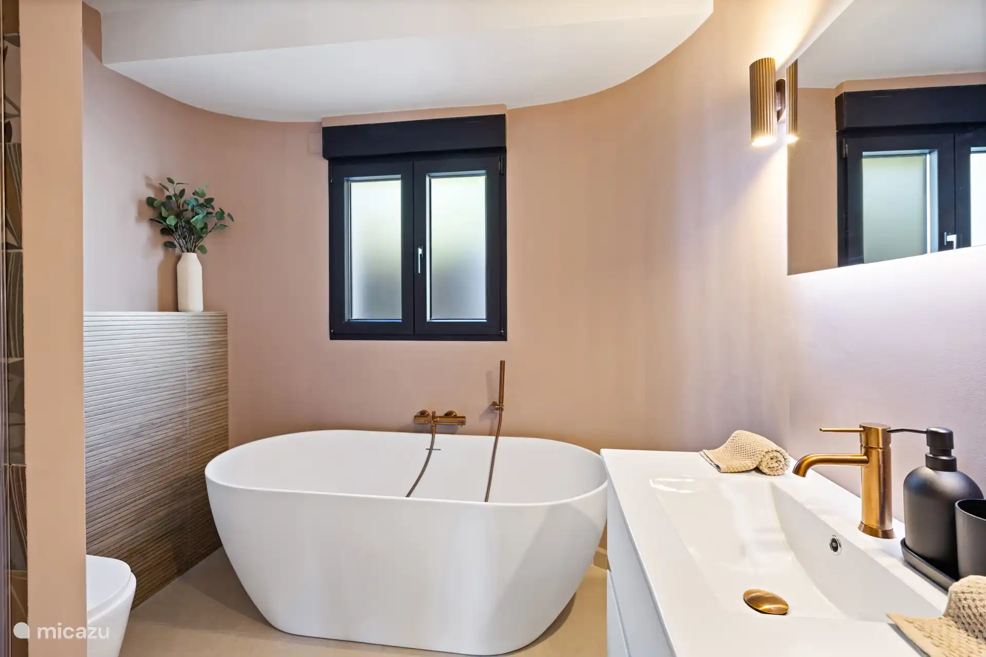 Vrijstaand bad met gouden accenten in een lichte, rustgevende badkamer  even helemaal tot rust komen na een dag strand