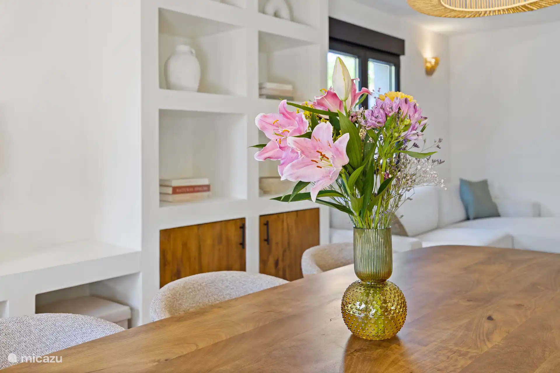 Eettafel met verse bloemen en zicht op de gezellige zithoek — de plek waar de dag samen wordt afgesloten