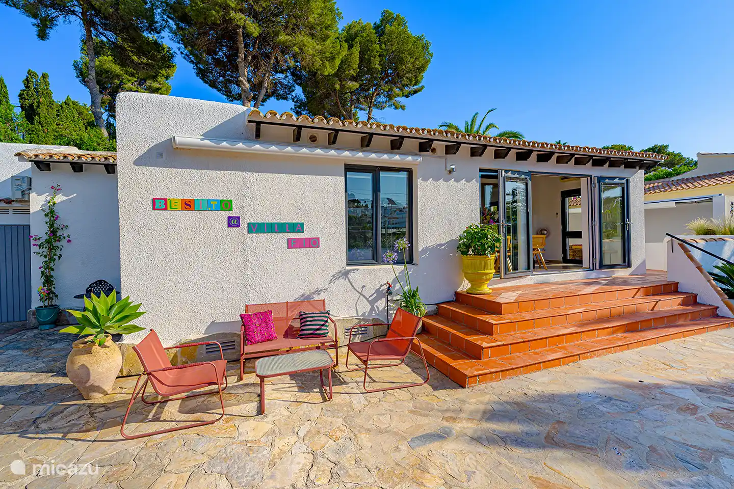 Frontansicht der Villa Fio mit sonniger Terrasse und Terrassentüren zum Wohnzimmer. Innen und außen verschmelzen hier nahtlos.