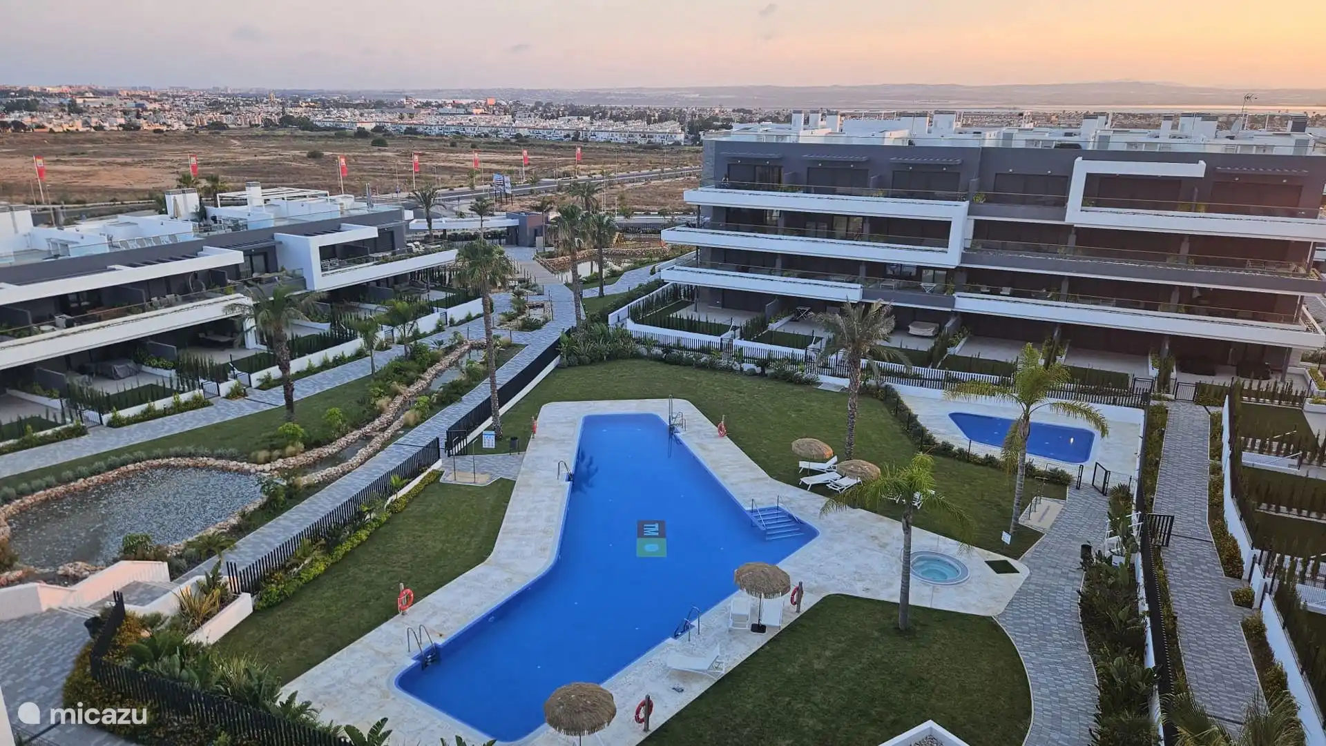 Blick vom Balkon. Das Schwimmbad verfügt über einen speziellen Stuhl für Behinderte, um das Schwimmbecken zu betreten. Neben dem Pool rechts ein beheizter Jacuzzi, direkt hinter einem Kinderbecken. 