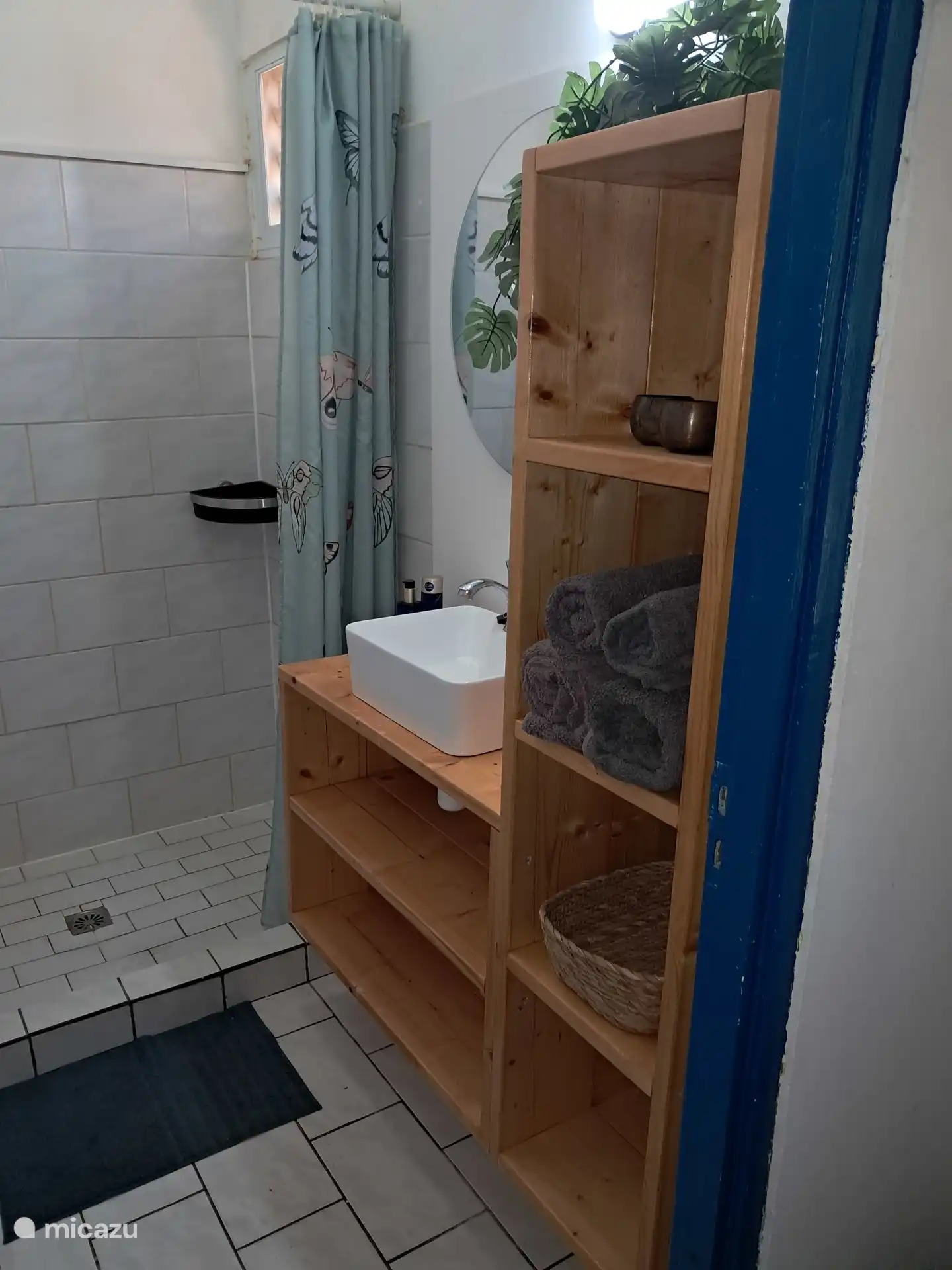 Baño ordenado y funcional con un lavabo de madera, un cuenco blanco montado en la superficie y un gran espejo redondo.