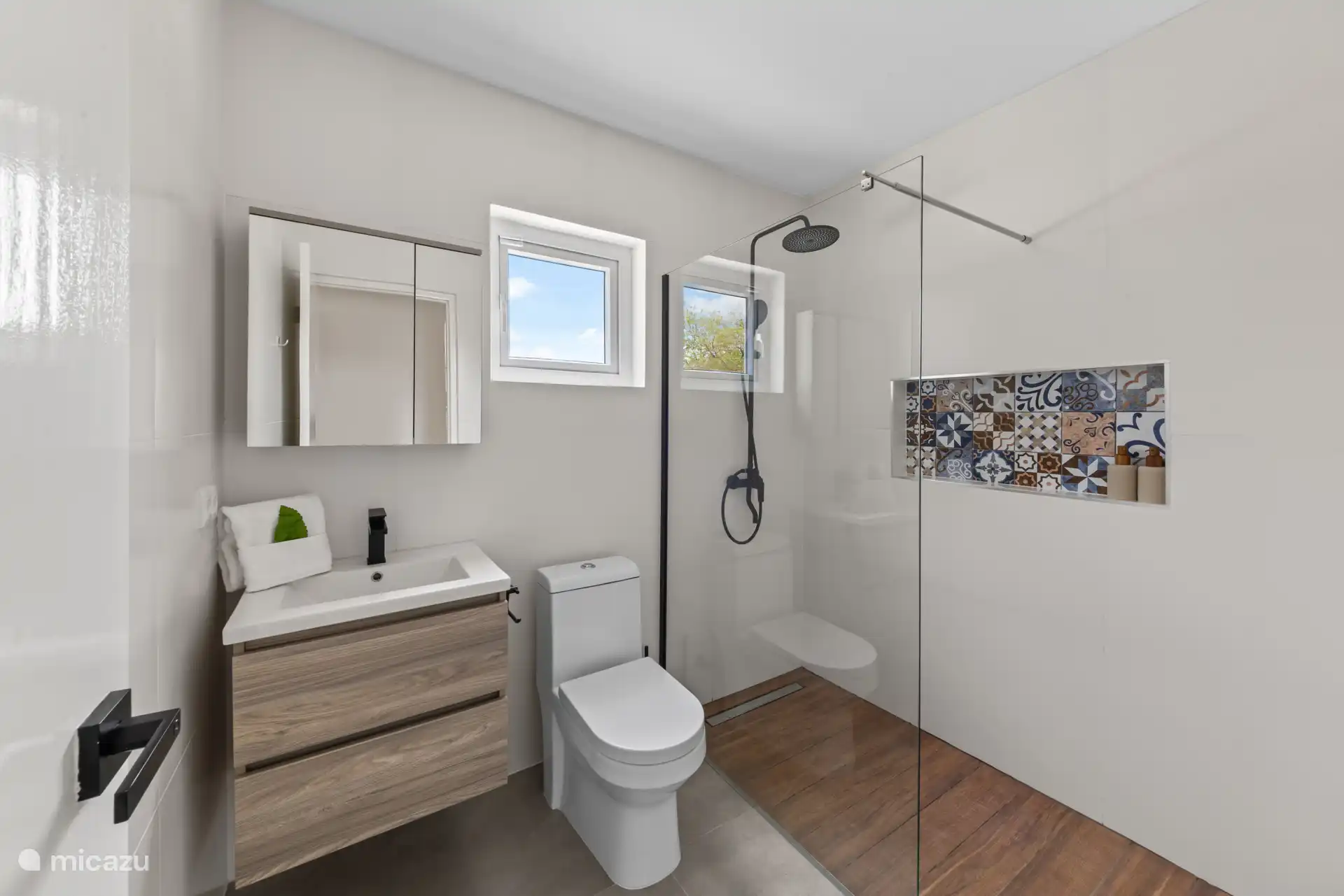De moderne badkamer is stijlvol ingericht en beschikt over een ruime inloopdouche met regendouche, een wastafelmeubel en toilet