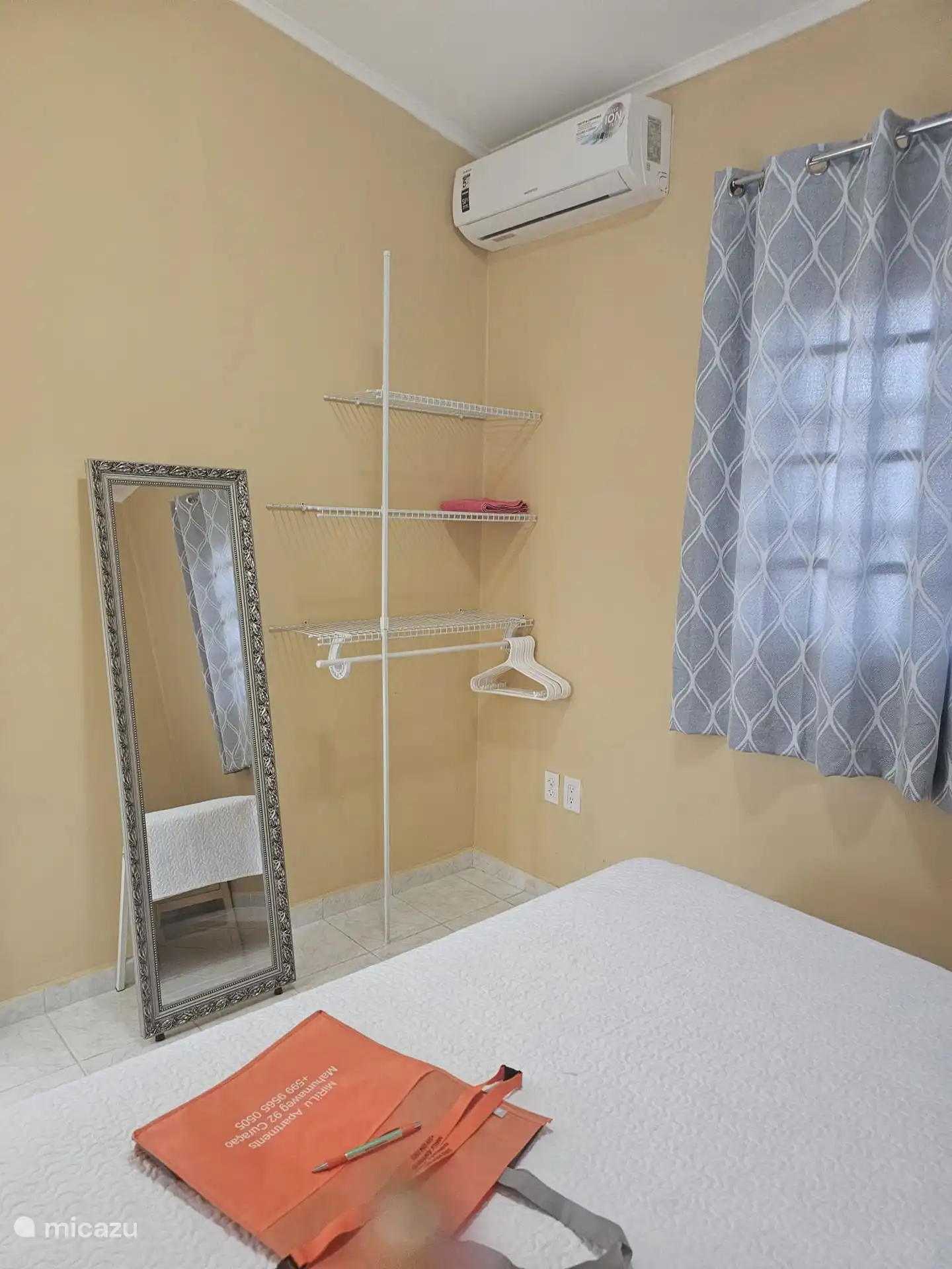 In the bedroom there is a mirror, a clothes rack with clothes hangers