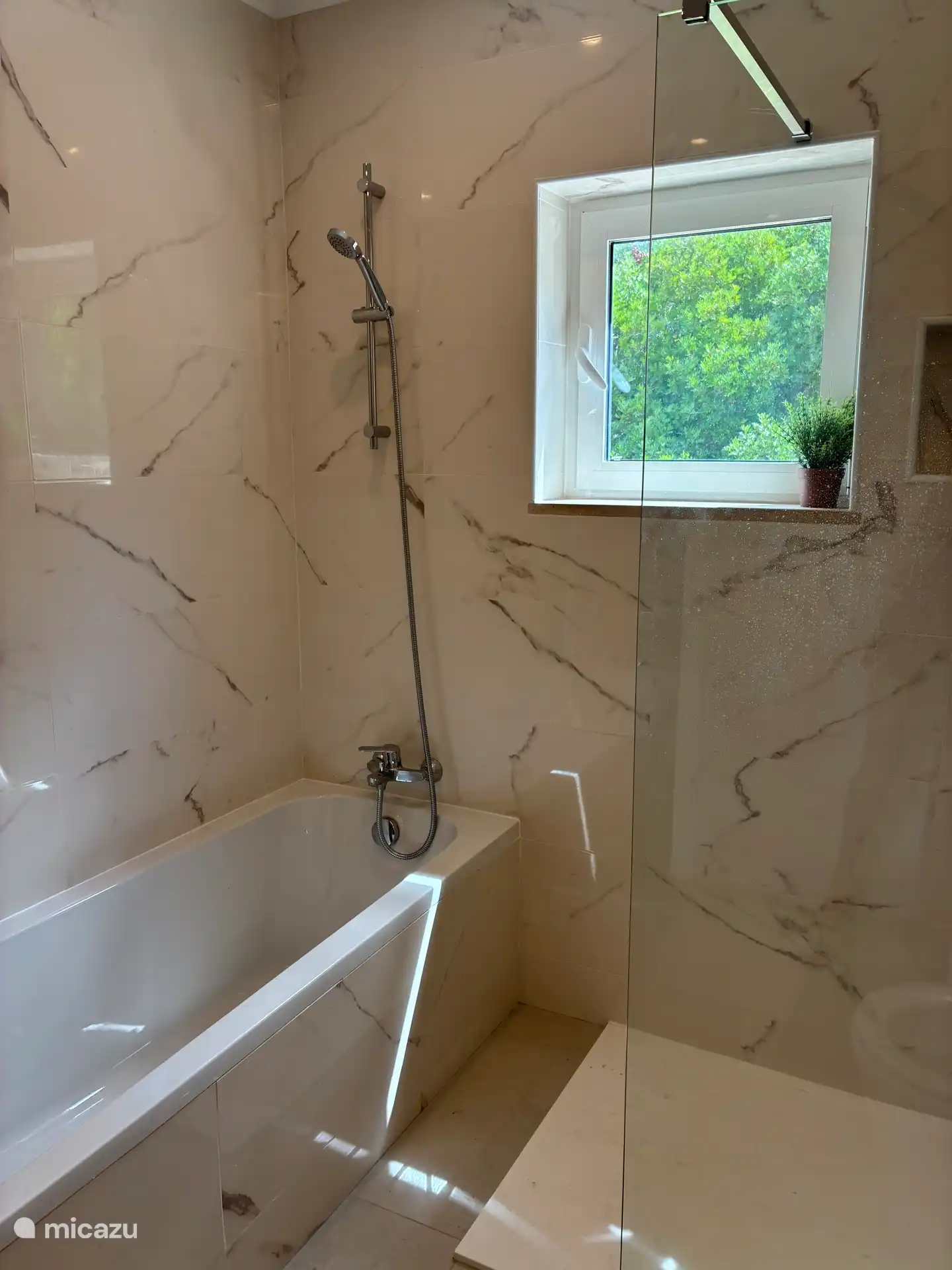 De badkamer heeft een handdouche en uitzicht op het groen.