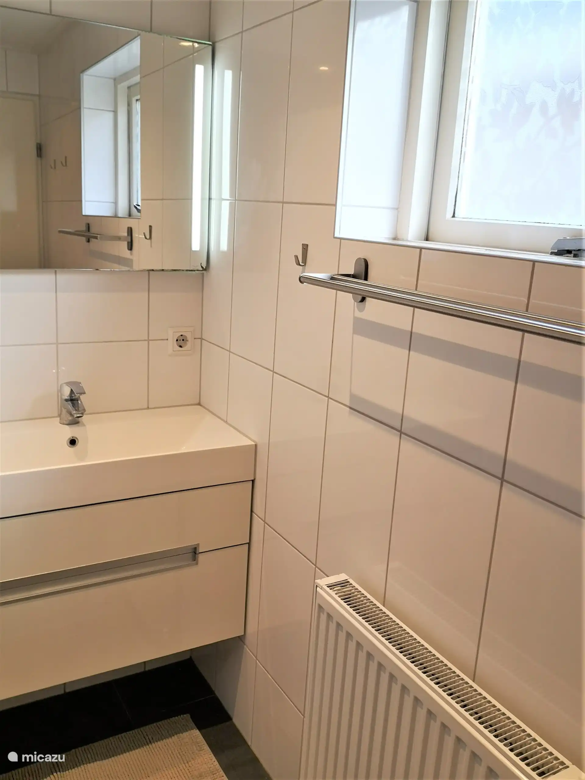 Badezimmer mit Waschbecken, Handtuchhalter, Heizkörper, Spiegel mit Beleuchtung und Kommode.
