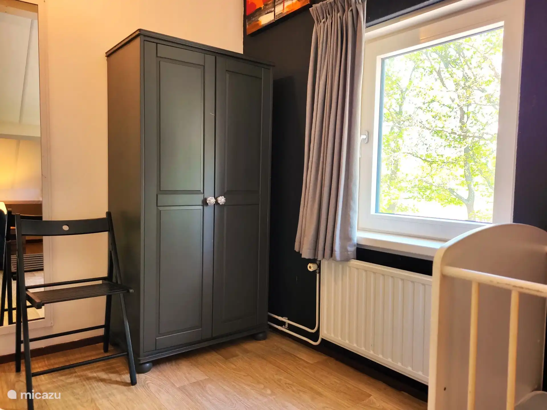 4. Schlafzimmer mit Kleiderschrank, Stuhl, Fenster vorne im Haus, Heizkörper, Spiegel.