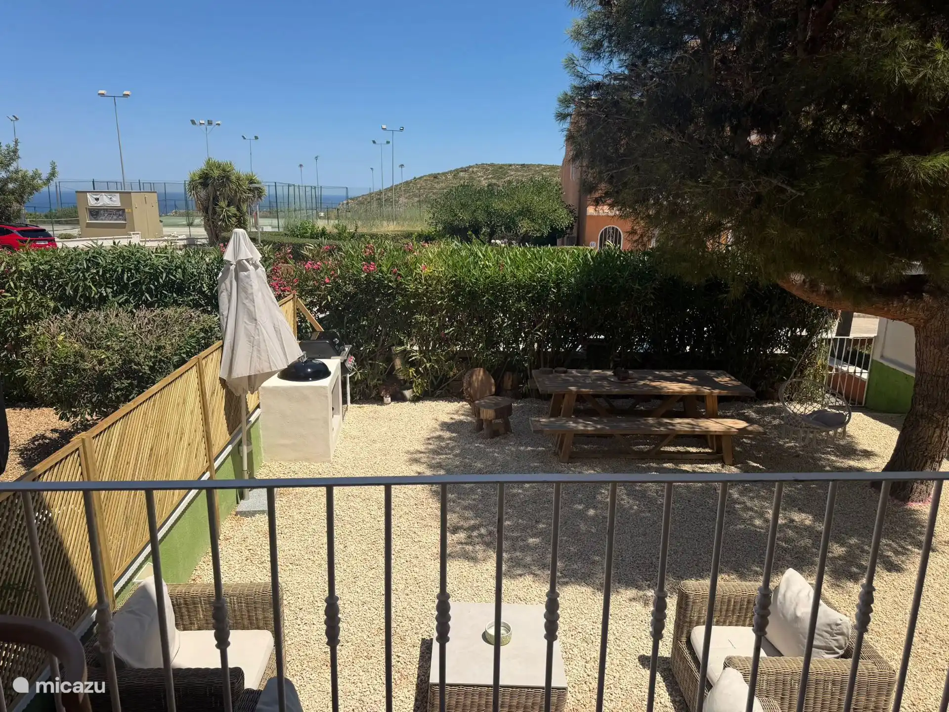 El jardín con zona de descanso, dos sombras, el hermoso árbol y la zona de barbacoa con su mesa para comer al aire libre.
