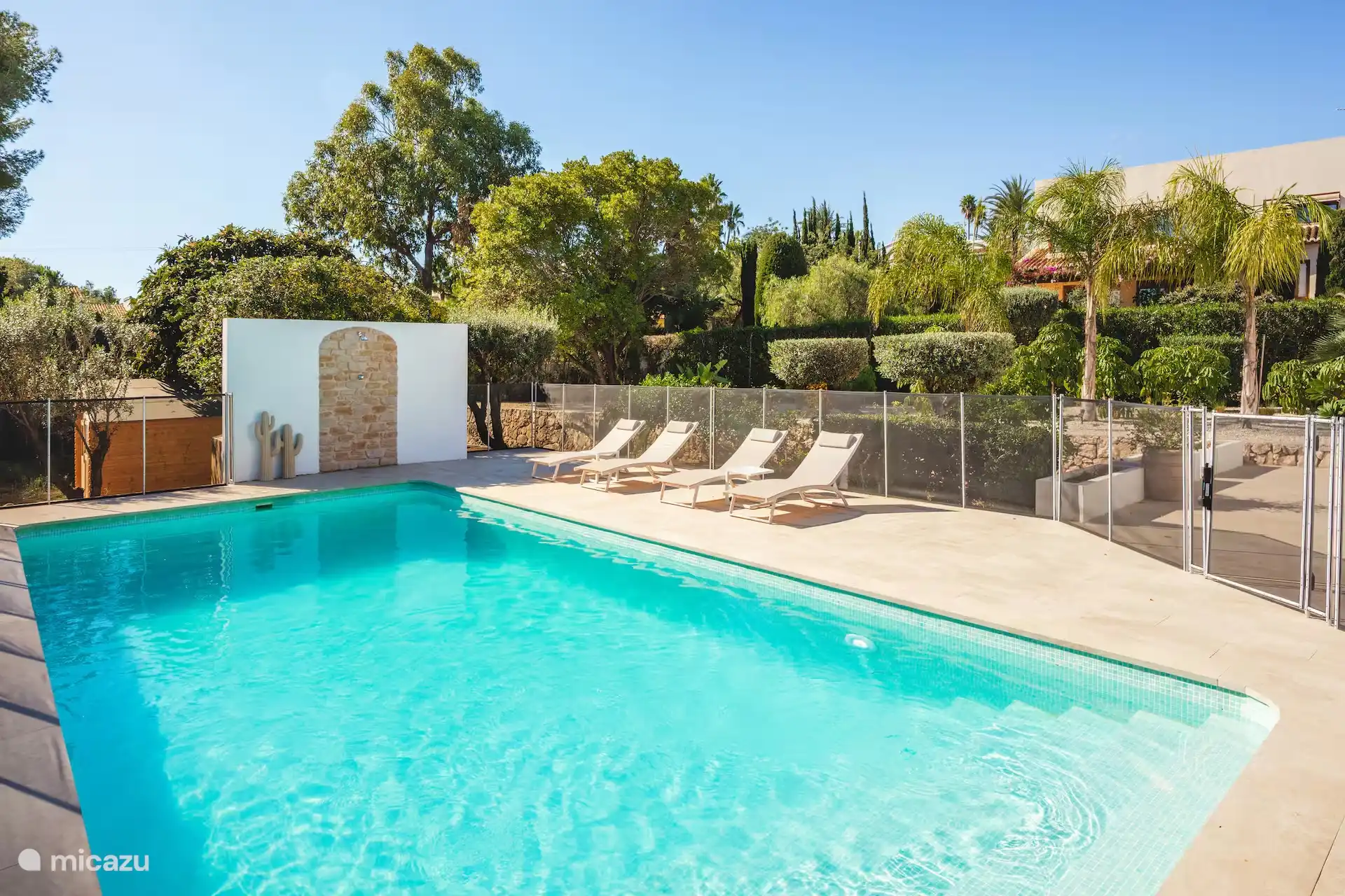 La piscine. La clôture de sécurité peut être retirée si désiré. Il y a une douche extérieure, des chaises longues, divers parasols et tables d’appoint. 