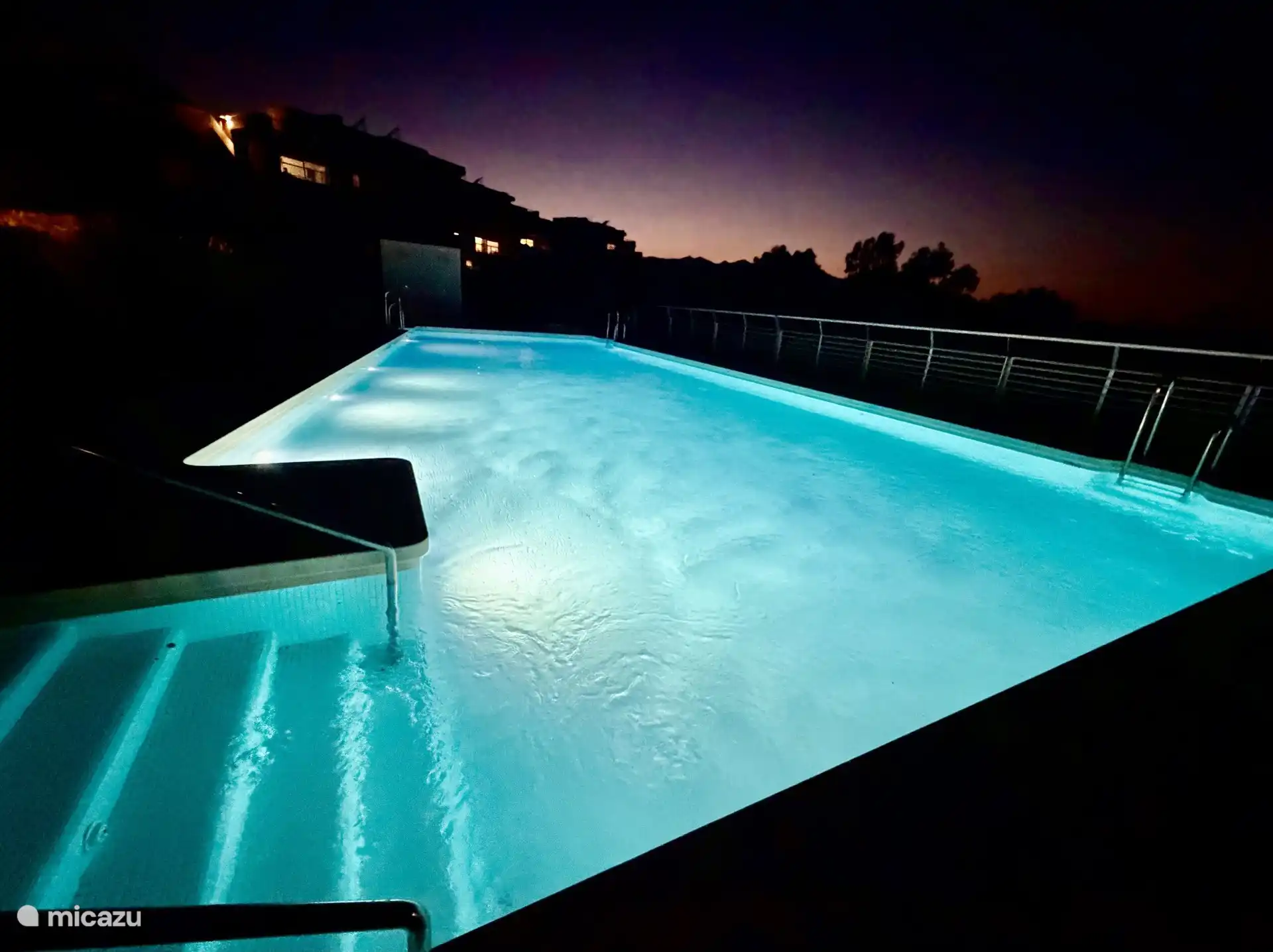 The communal swimming pool of the complex at dusk, with the underwater lights on.
