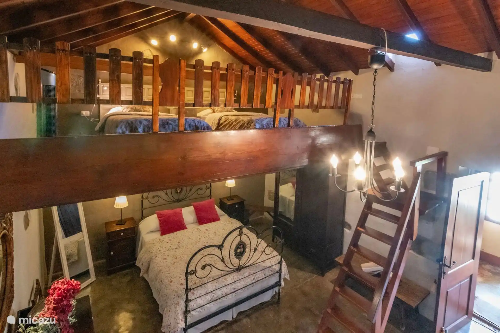 Slaapkamer met smeedijzeren bed onder een houten mezzanine