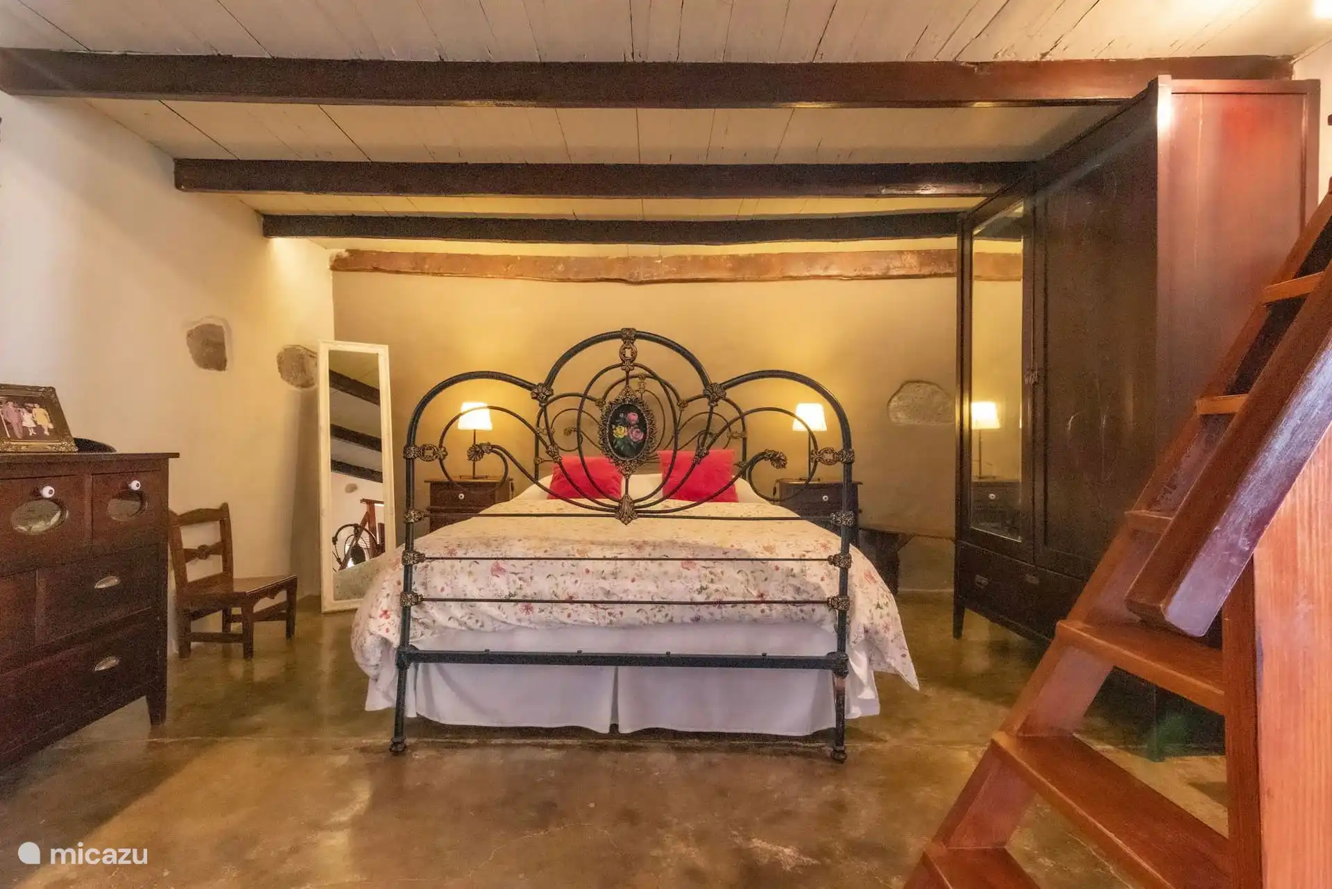 Slaapkamer met smeedijzeren tweepersoonsbed en mezzanine, rustieke sfeer