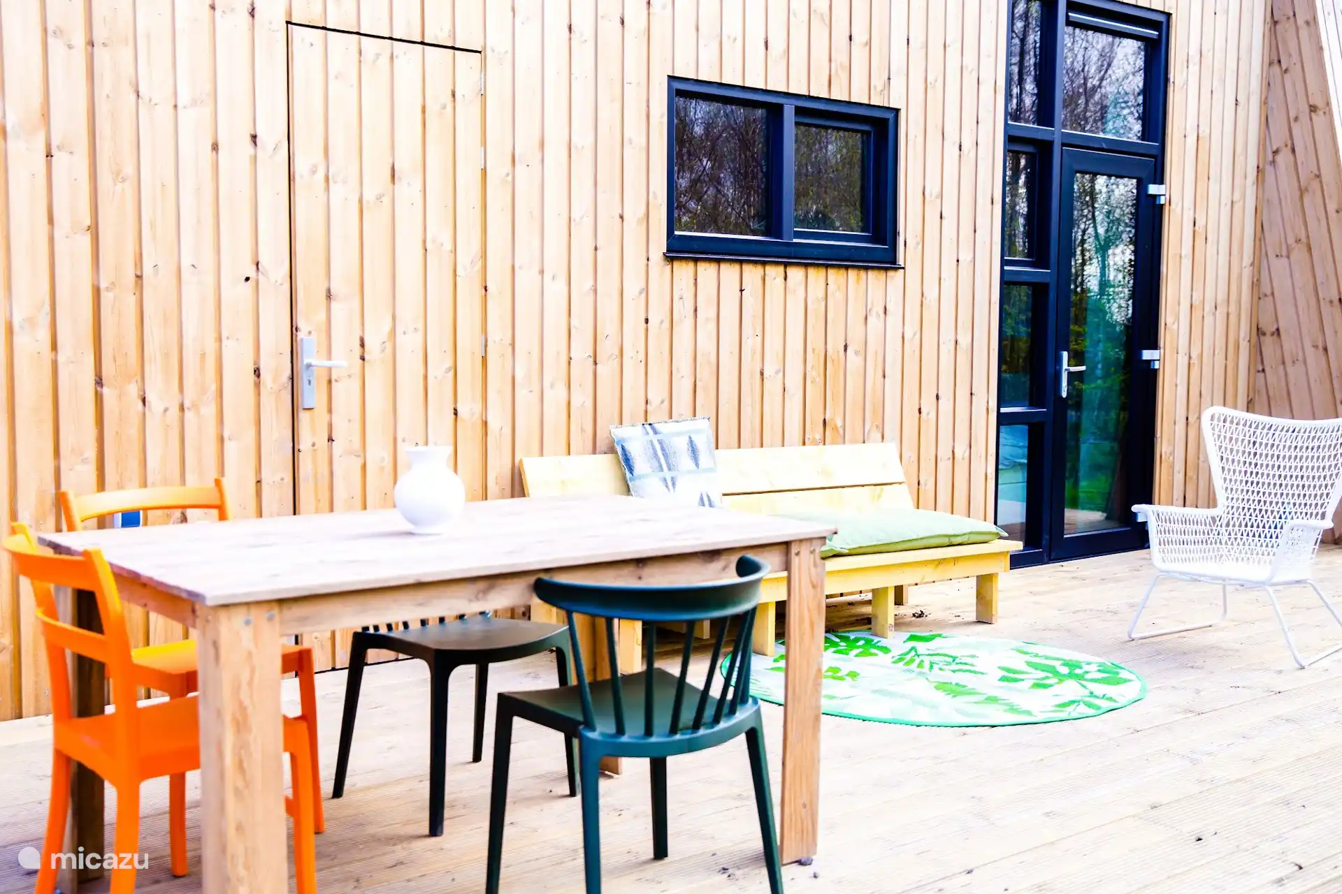 Terras aan de zijkant van de lodge met houten eettafel, kleurrijke stoelen en loungebank.
