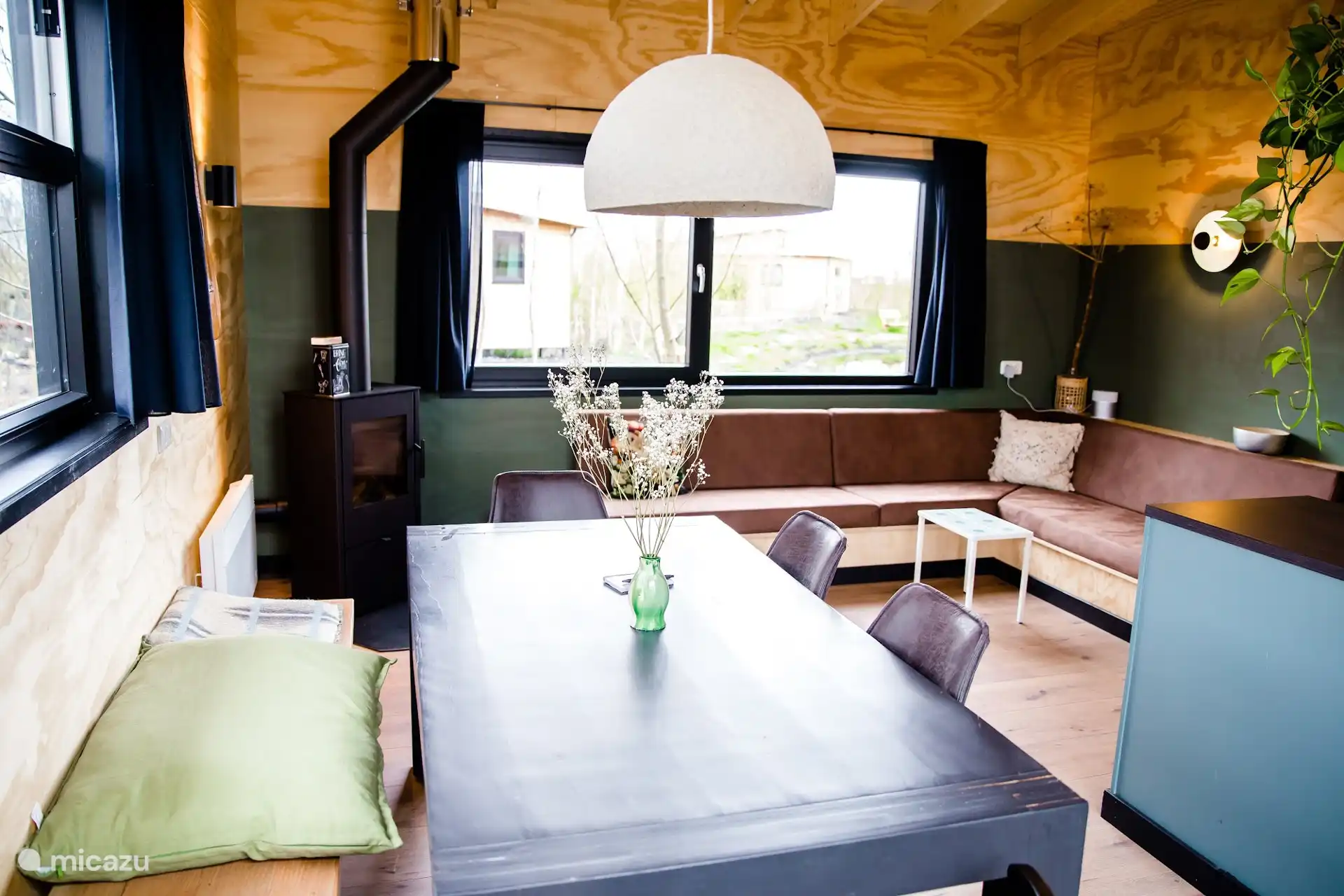 Eettafel bij het raam met bankje, hanglamp en uitzicht op het groen.