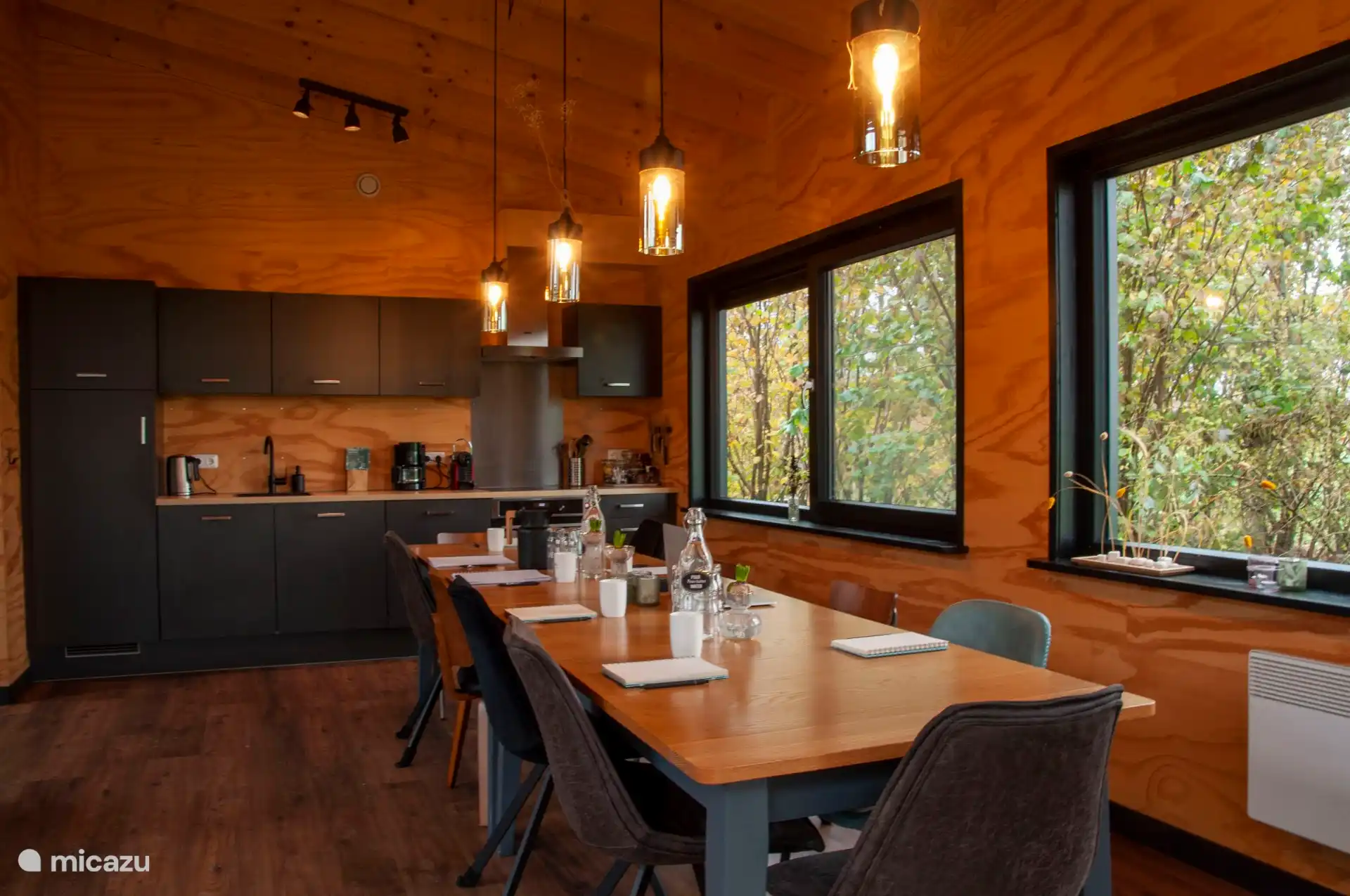 Open keuken met lange eettafel, sfeervol verlicht met hanglampen.