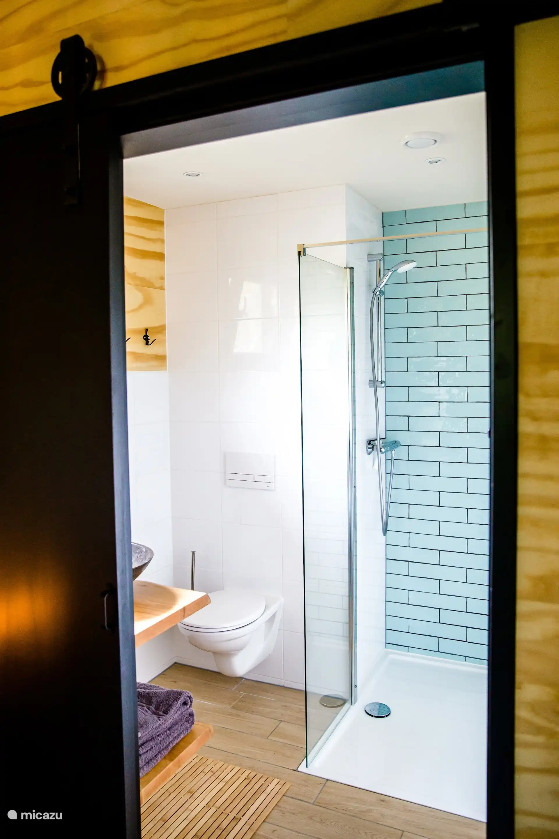 Toilet in de badkamer met inloopdouche, warme houten details en moderne afwerking.