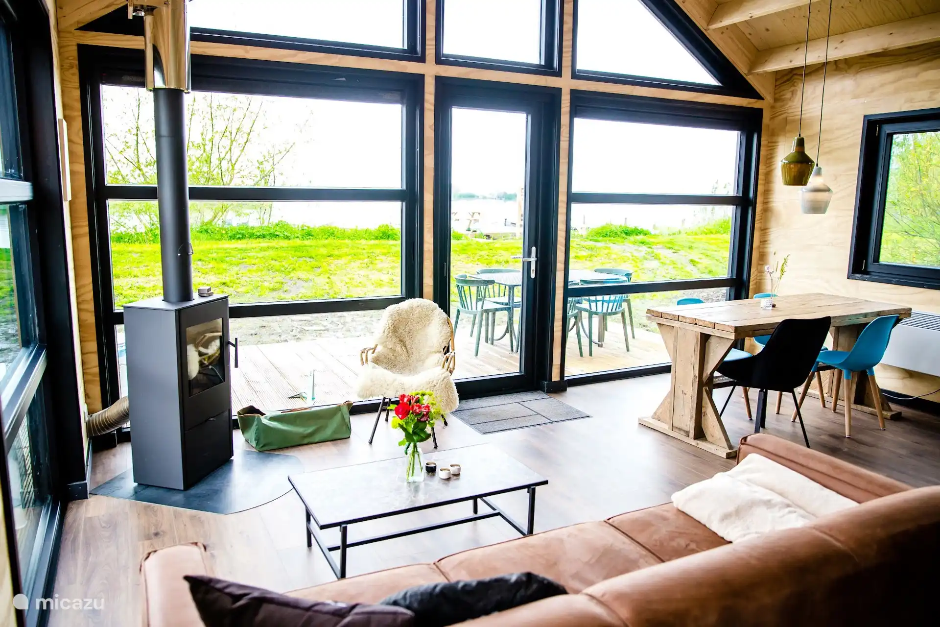 Lichte woonkamer met houtkachel, zithoek en eettafel bij de grote ramen.