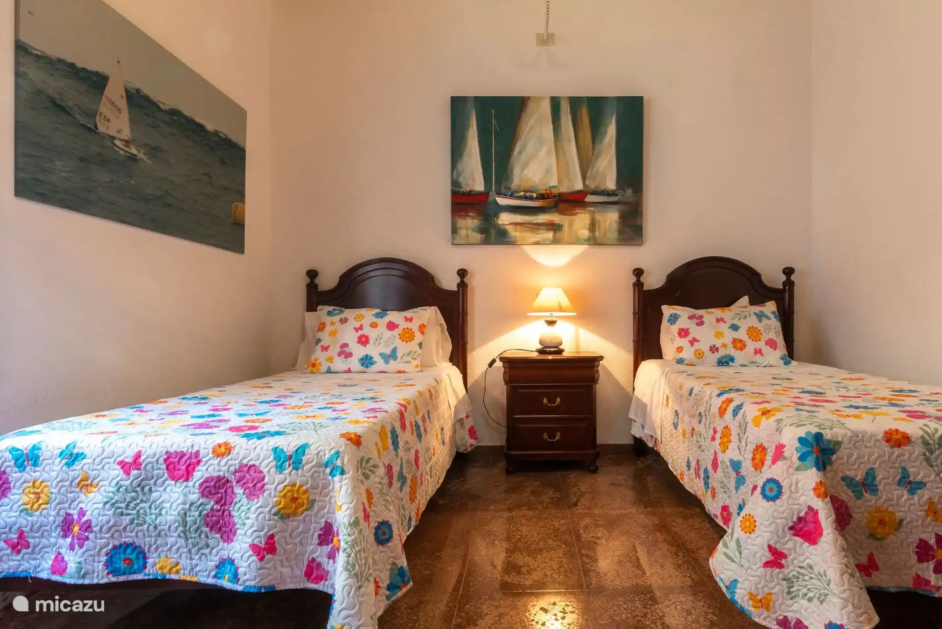 Slaapkamer met twee eenpersoonsbedden en zeemansschilderijen.