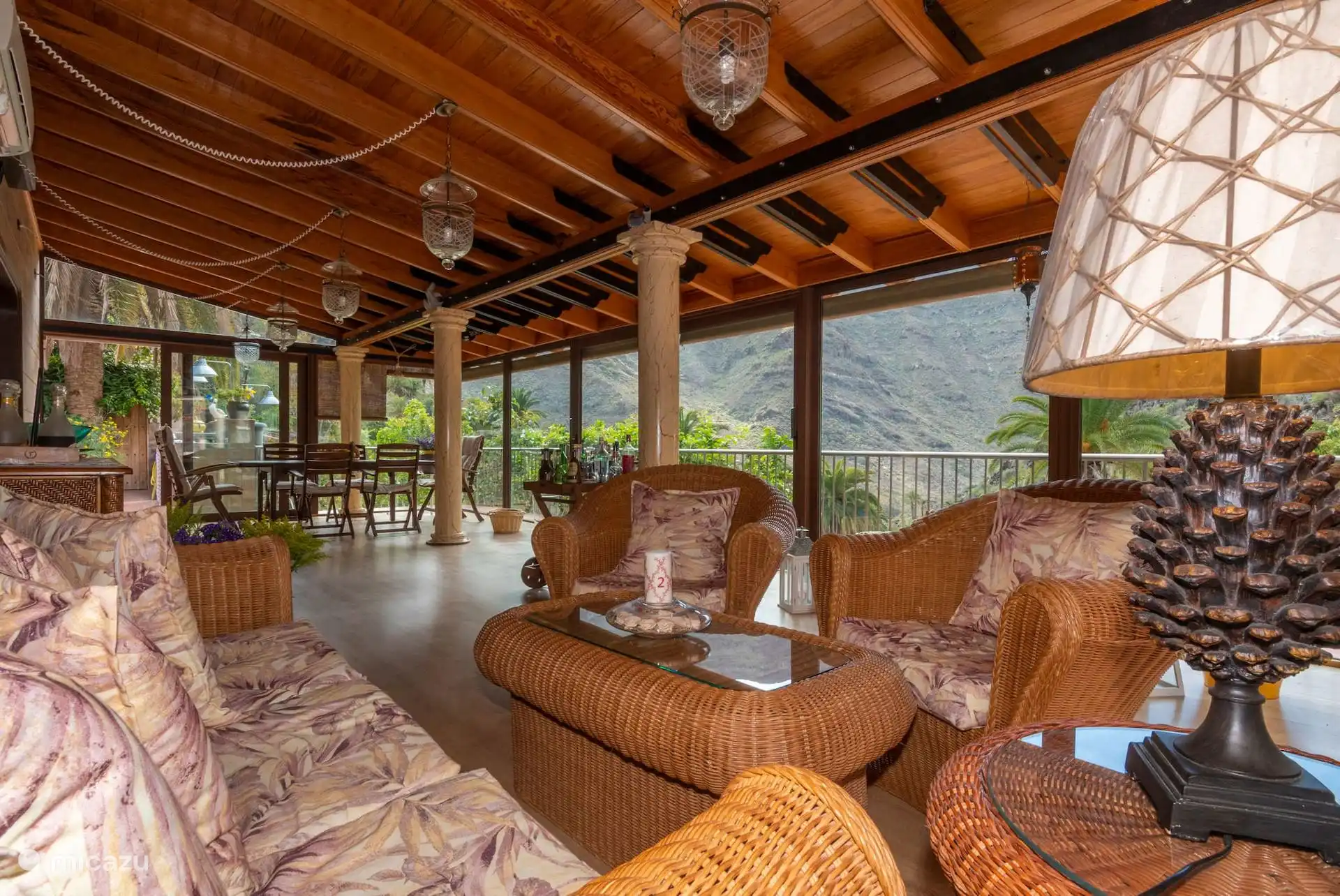Glazen terras met houten dak en stenen zuilen, met rotan fauteuils en uitzicht op de kloof.