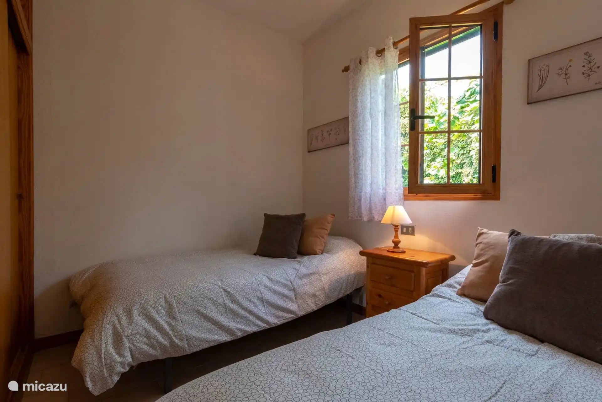 Otra vista del dormitorio de dos camas, con mesilla y lámpara.