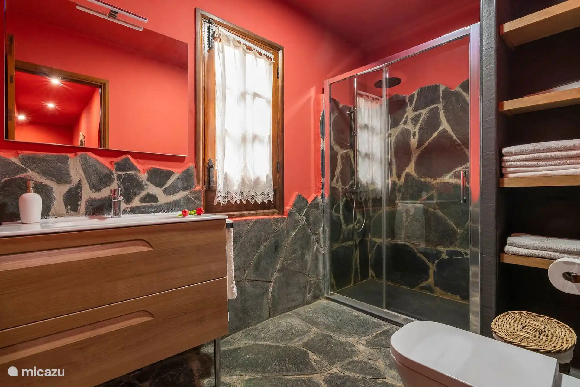 Baño con ducha de obra en piedra, mampara y lavabo de madera.