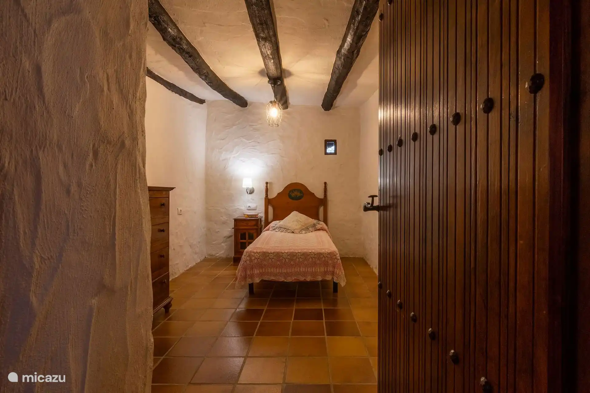 Dormitorio individual con muro de piedra y puerta de madera.