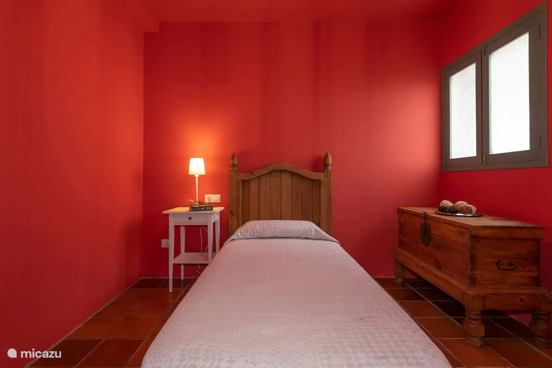 Dormitorio individual con mesilla y arcón de madera.