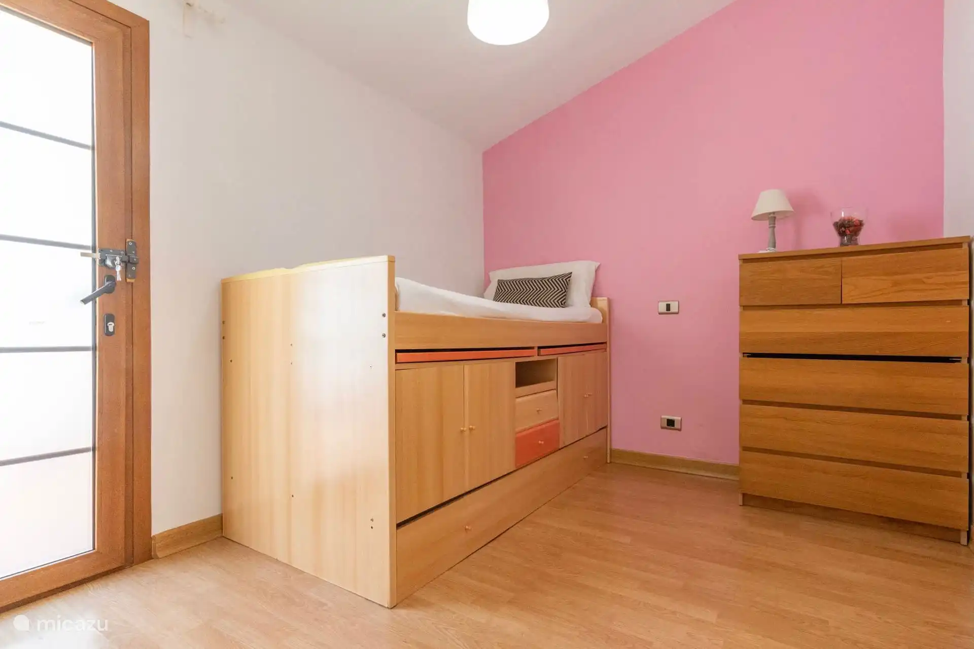 Dormitorio con cama compacta y cajones, en tonos rosas.