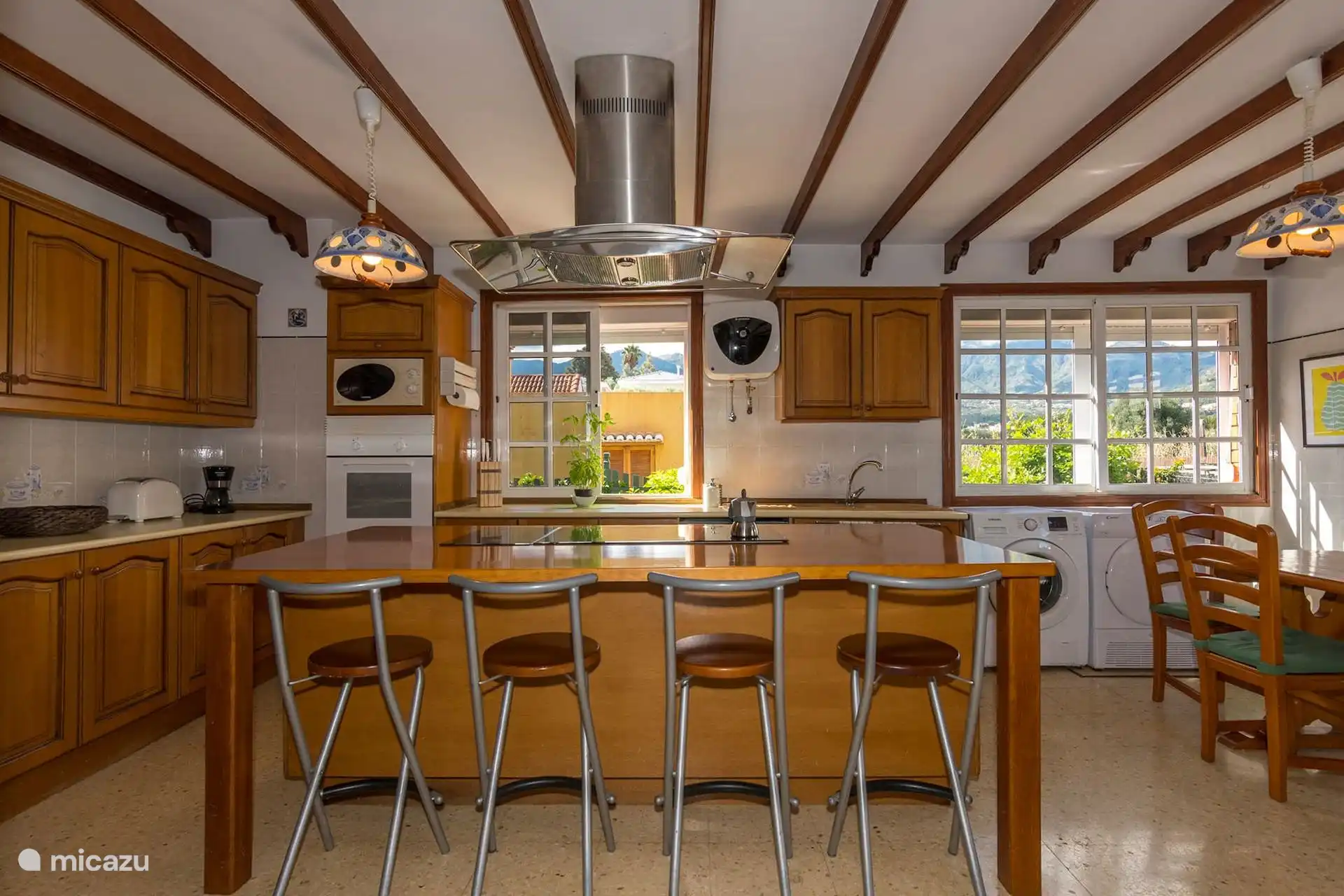 Cocina con horno, vitrocerámica y barra de desayuno con taburetes.