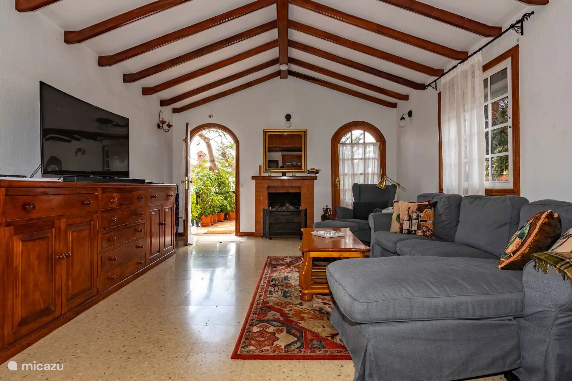 Salón con televisión, chimenea y puertas de arco al patio.
