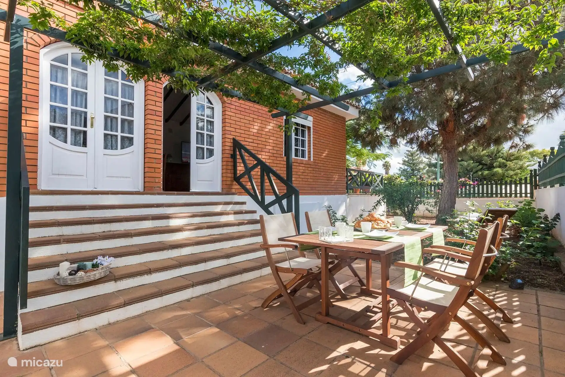 Escalera de entrada bajo la pérgola, con la mesa del patio preparada.