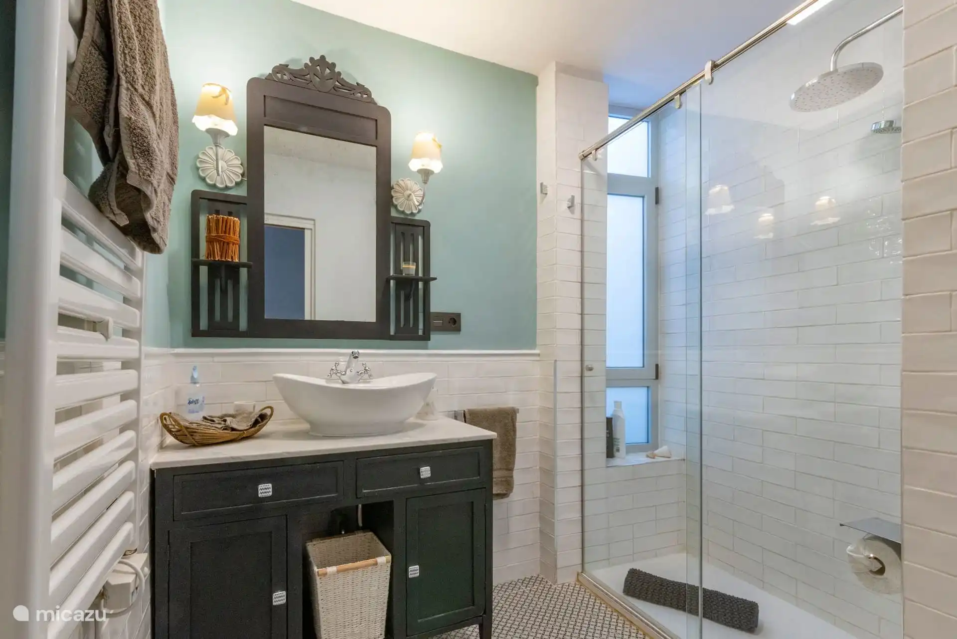 Baño con lavabo sobre mueble, espejo antiguo y radiador toallero.