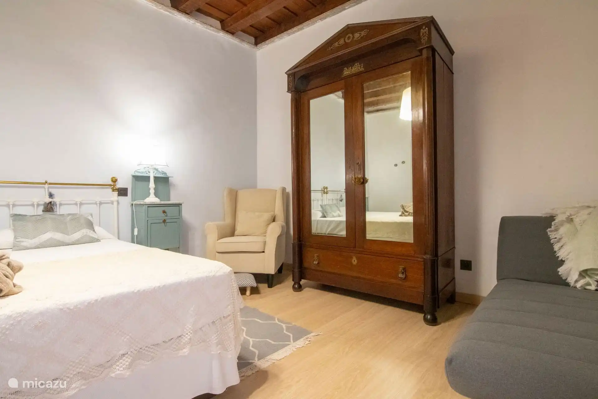 Otra vista del dormitorio, con sillón gris y armario de época.